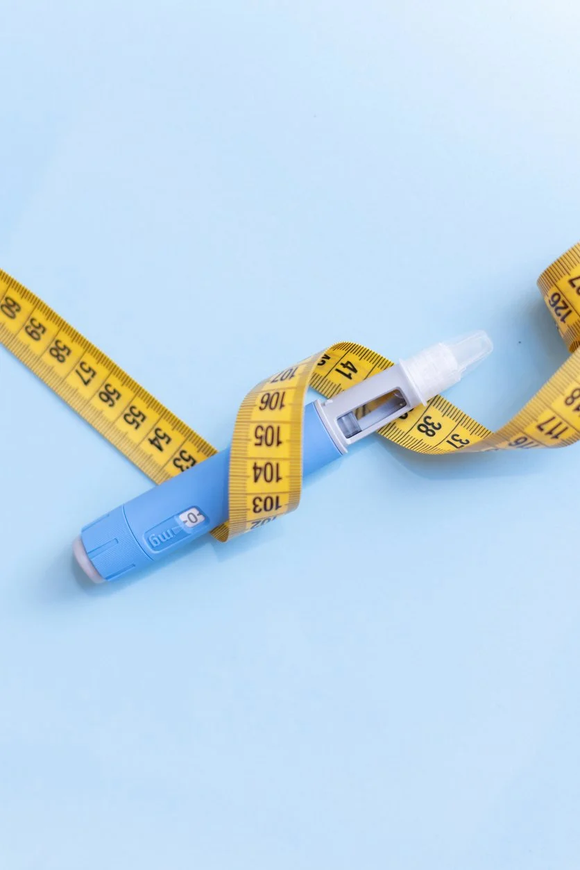 Weight loss injection pen wrapped in a yellow measuring tape on blue background.