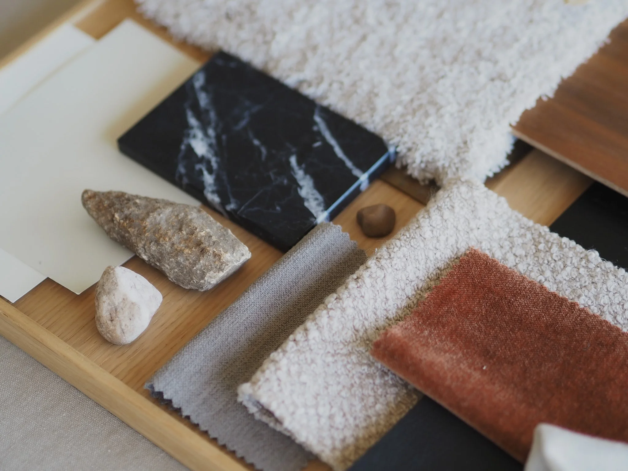 Close-up of interior design samples including fabric swatches, stone tiles, and a marble tile on a wooden tray.