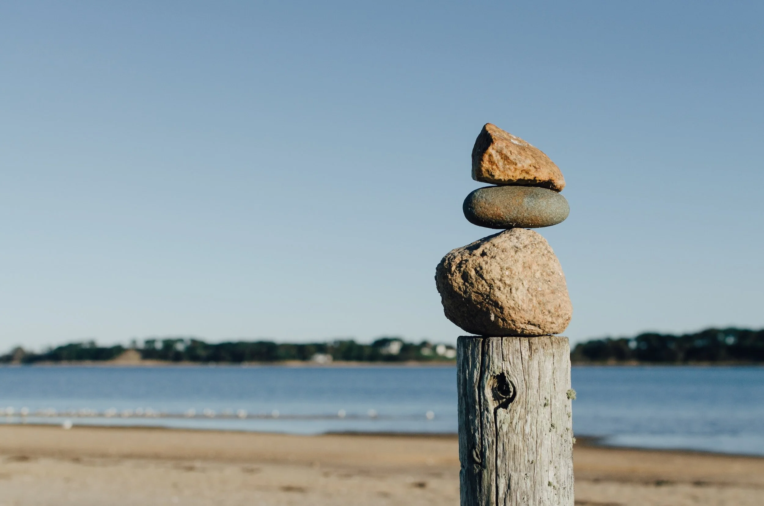 Stacked rocks on a wooden post by a beach.