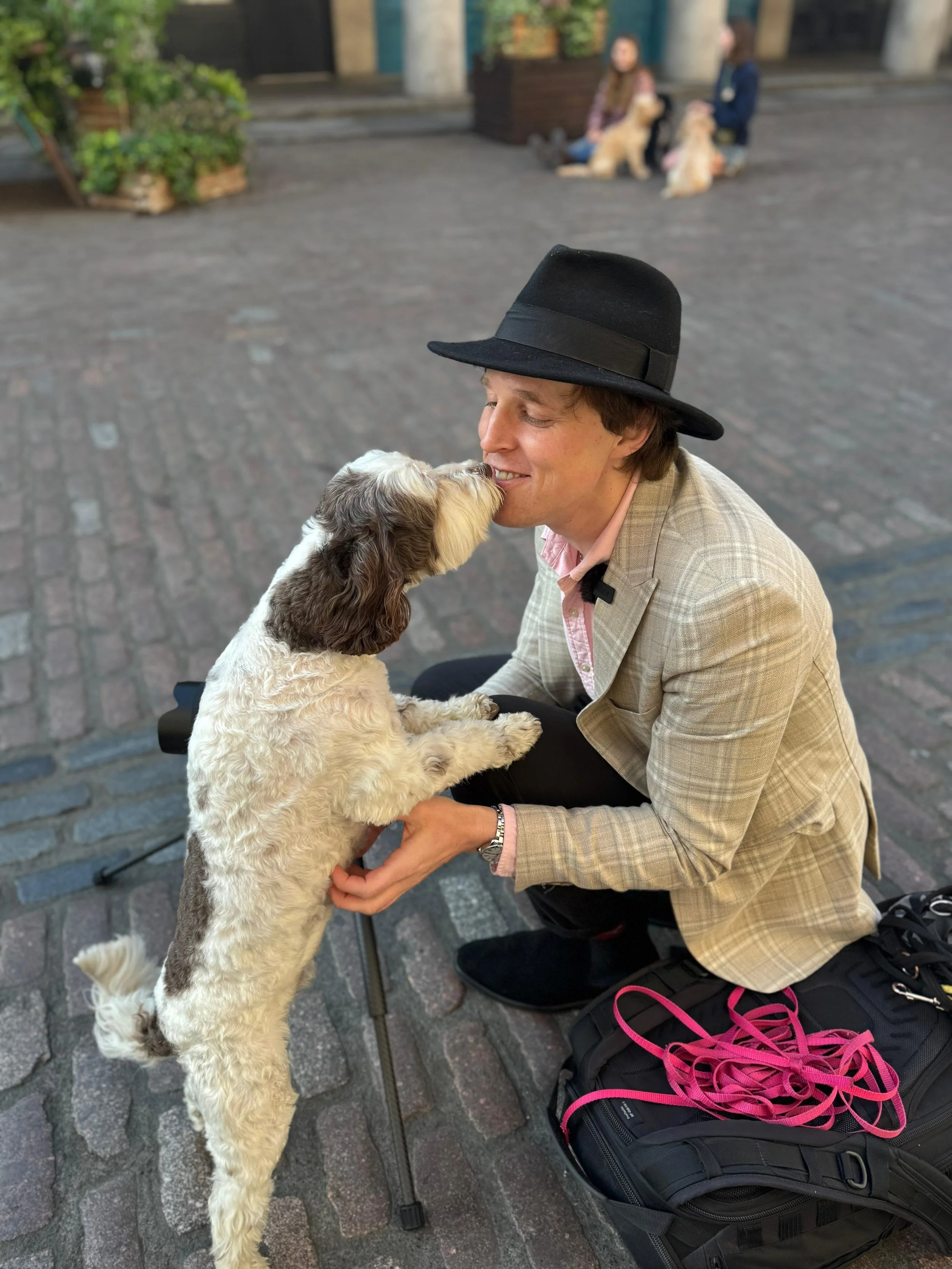 London dog photographer Andrew Raven kneeling on a cobbled street as a black and white dog stands up to greet him during a warm behind the scenes moment at a private photography session.