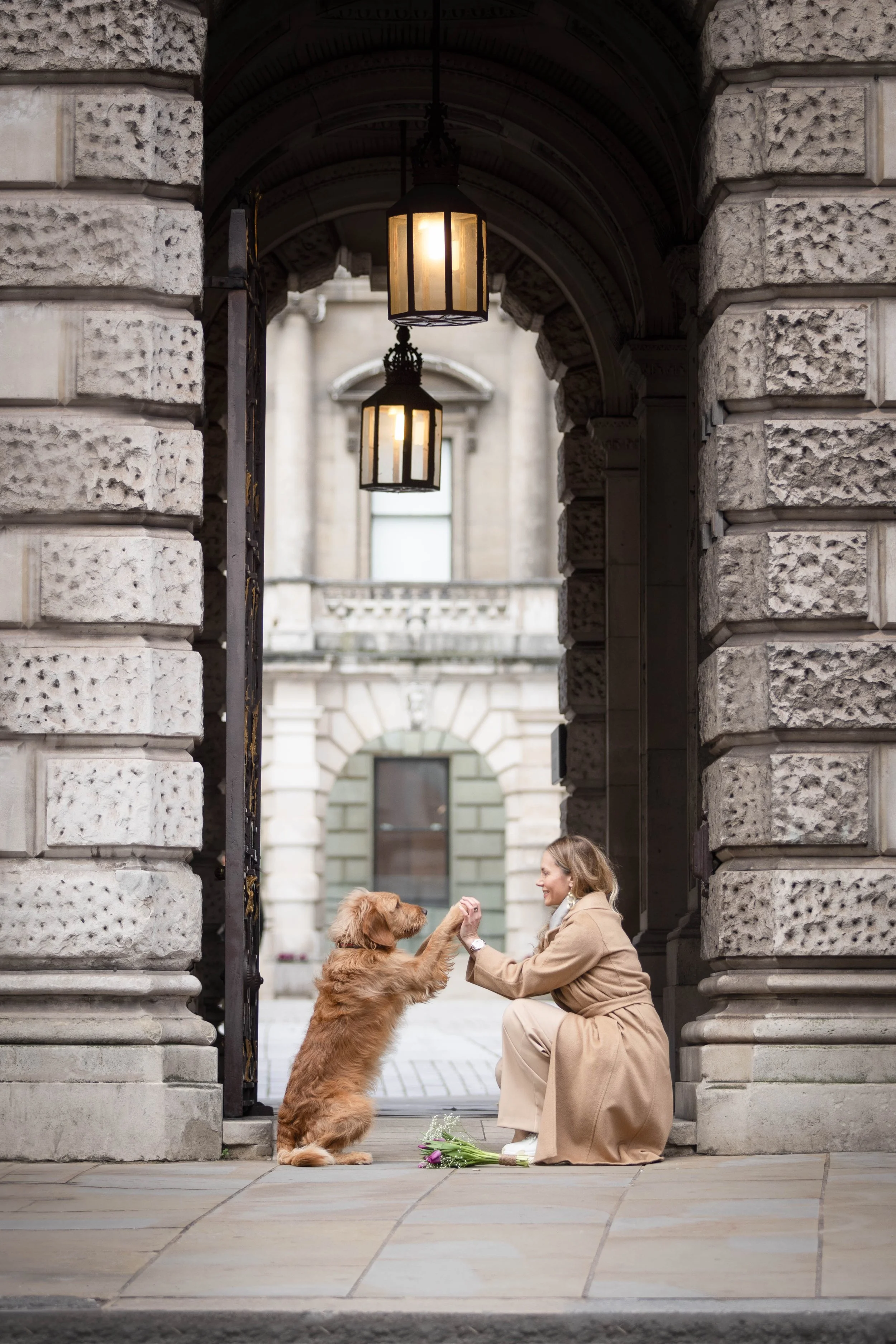 Fine art dog photograph by Andrew Raven of a Goldendoodle placing a paw in his owner's hand beneath a lantern-lit archway in Mayfair, London