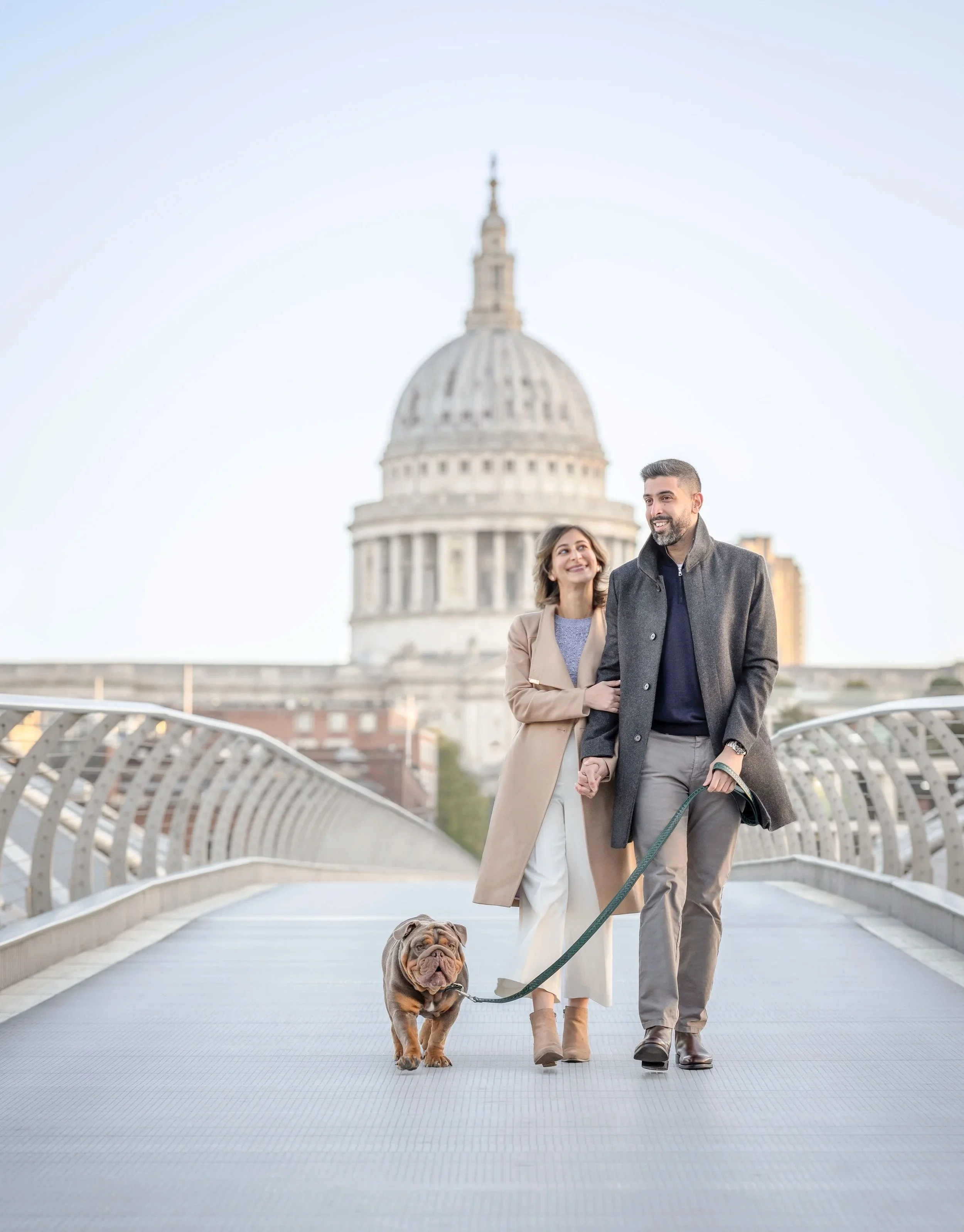 Couple walking across Millennium Bridge with their bulldog, with St Paul’s Cathedral in the background, during a private dog photography session in London.