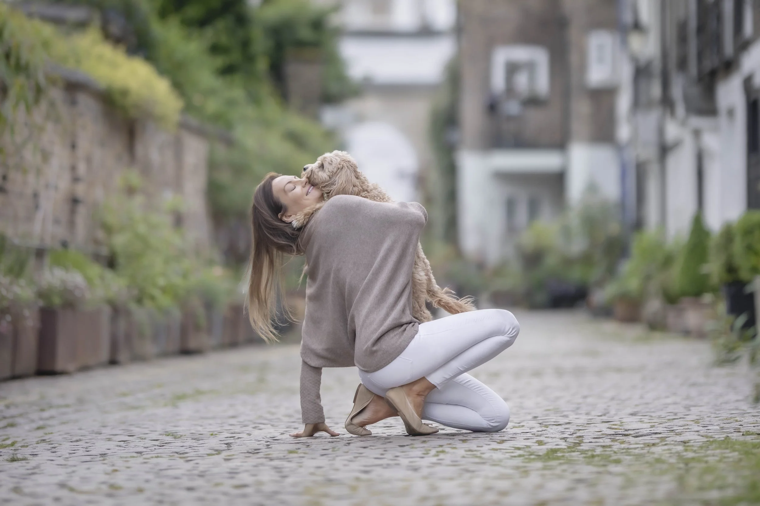 Woman cuddling her apricot doodle on a quiet cobbled mews in Kensington, London, during a natural owner and dog photography session.