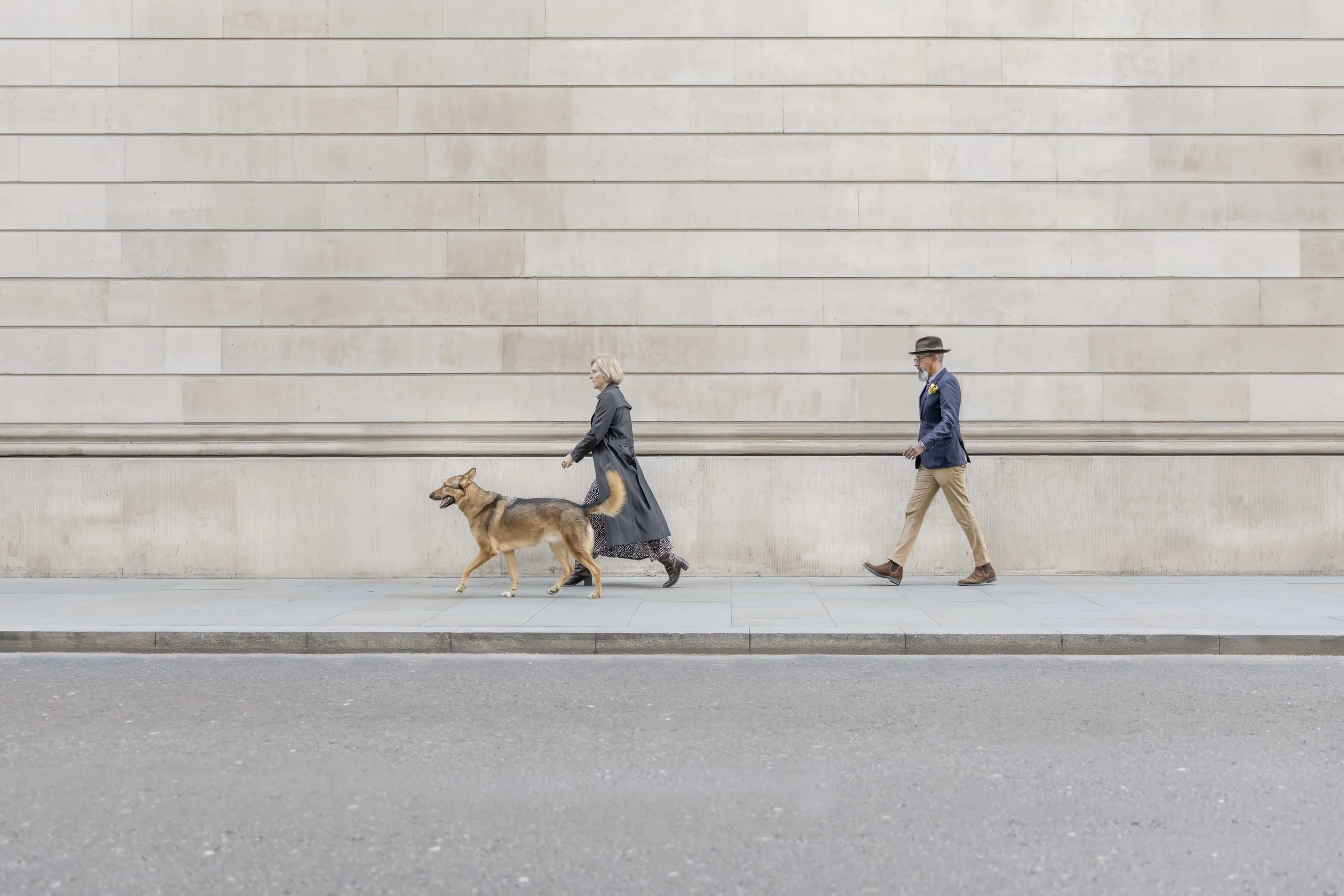 Couple walking with their rescue German Shepherd Husky mix beside the grand architecture of the City of London during a natural family and dog photography session.