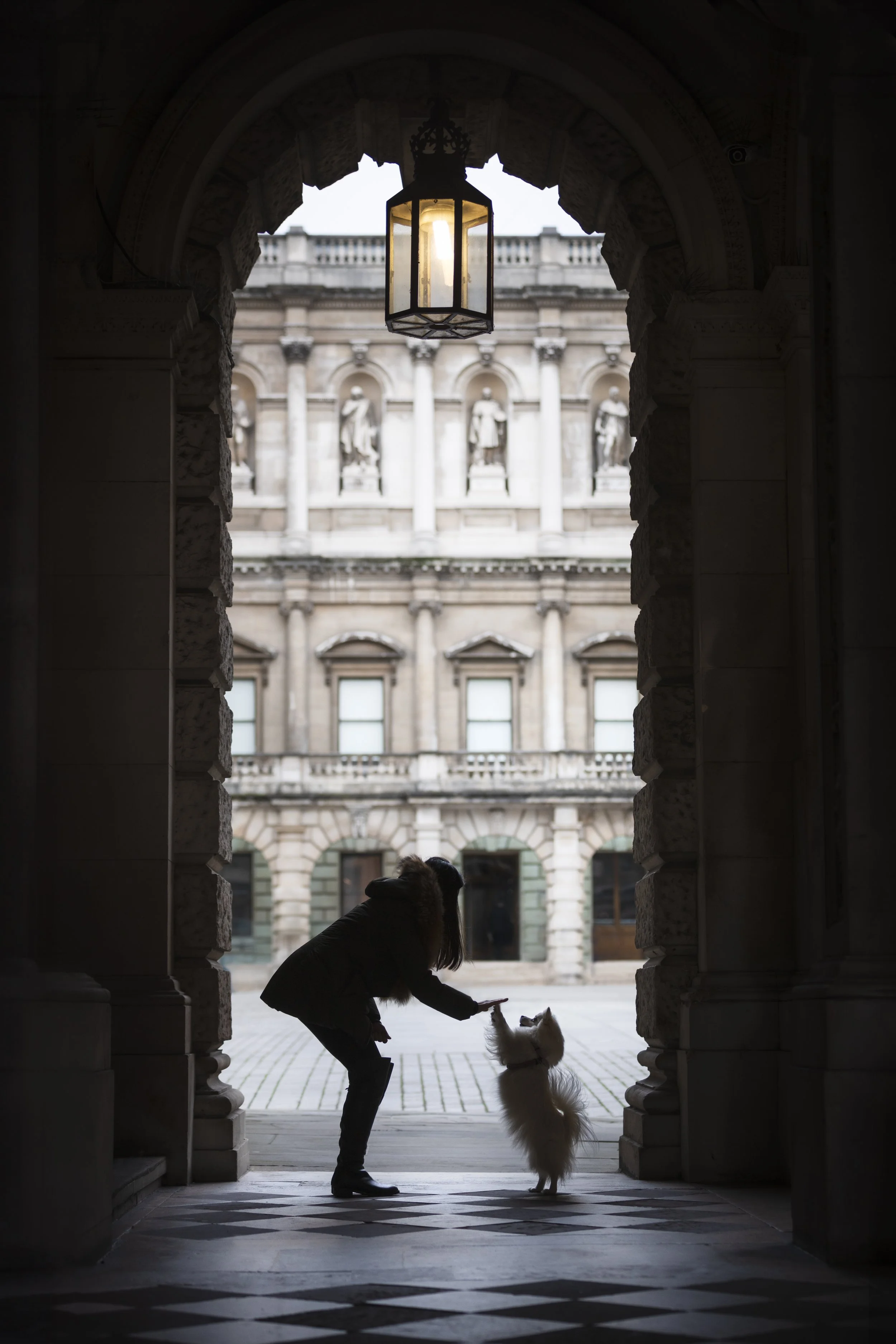 Toy American Eskimo Kiki Bear with their owner beneath an archway during a dog photography session in Mayfair, London, photographed by Andrew Raven.