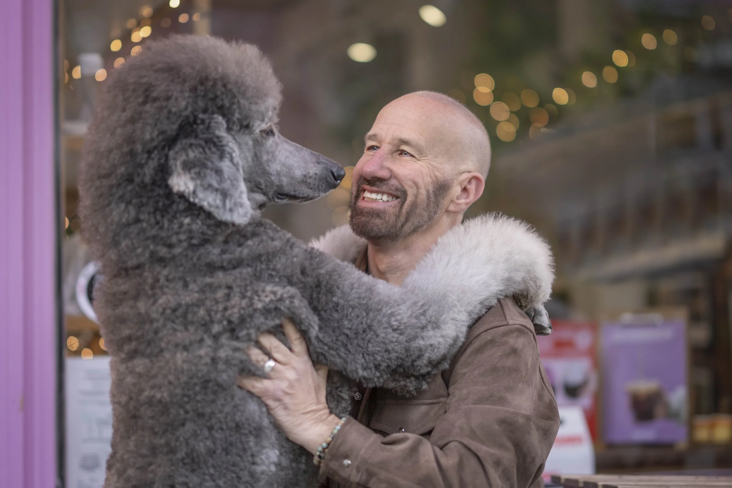 Man smiling while holding his grey Standard Poodle outside a Notting Hill café during a dog friendly day out and private dog photography session in London.