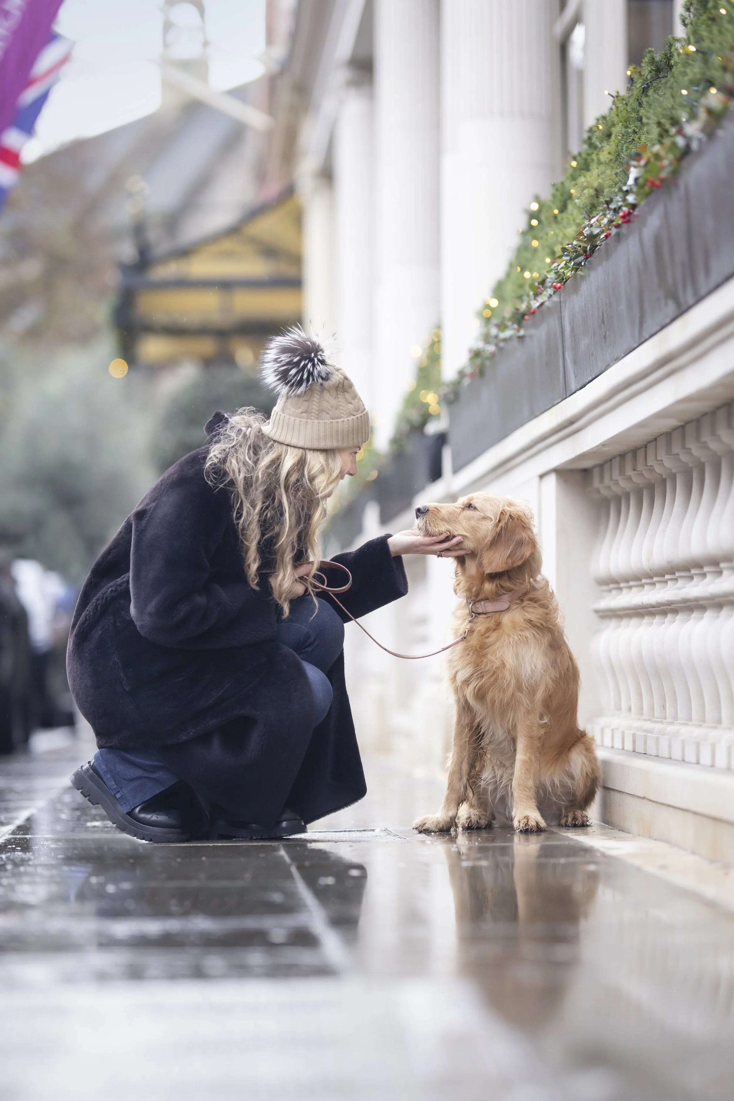 Woman crouching beside her Golden Retriever on a rain washed pavement in Mayfair, London, sharing a heartfelt moment during a natural pet and owner photography session.
