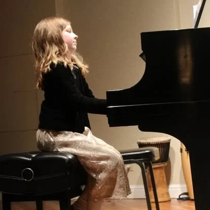 A young girl playing a grand piano in a room.