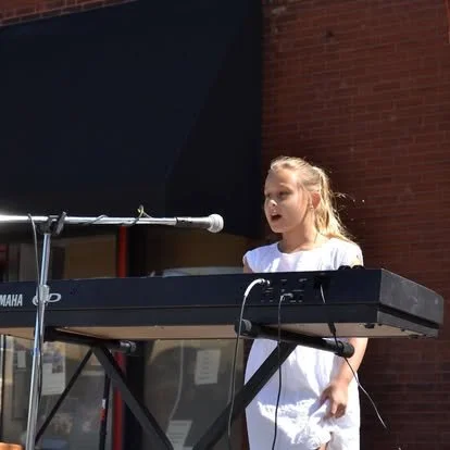 A young vocal student singing out at an outdoor festival 