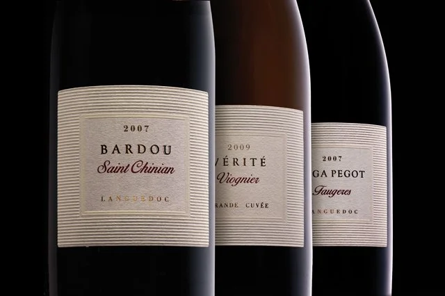 Three bottles of red wine with white labels against a black background.