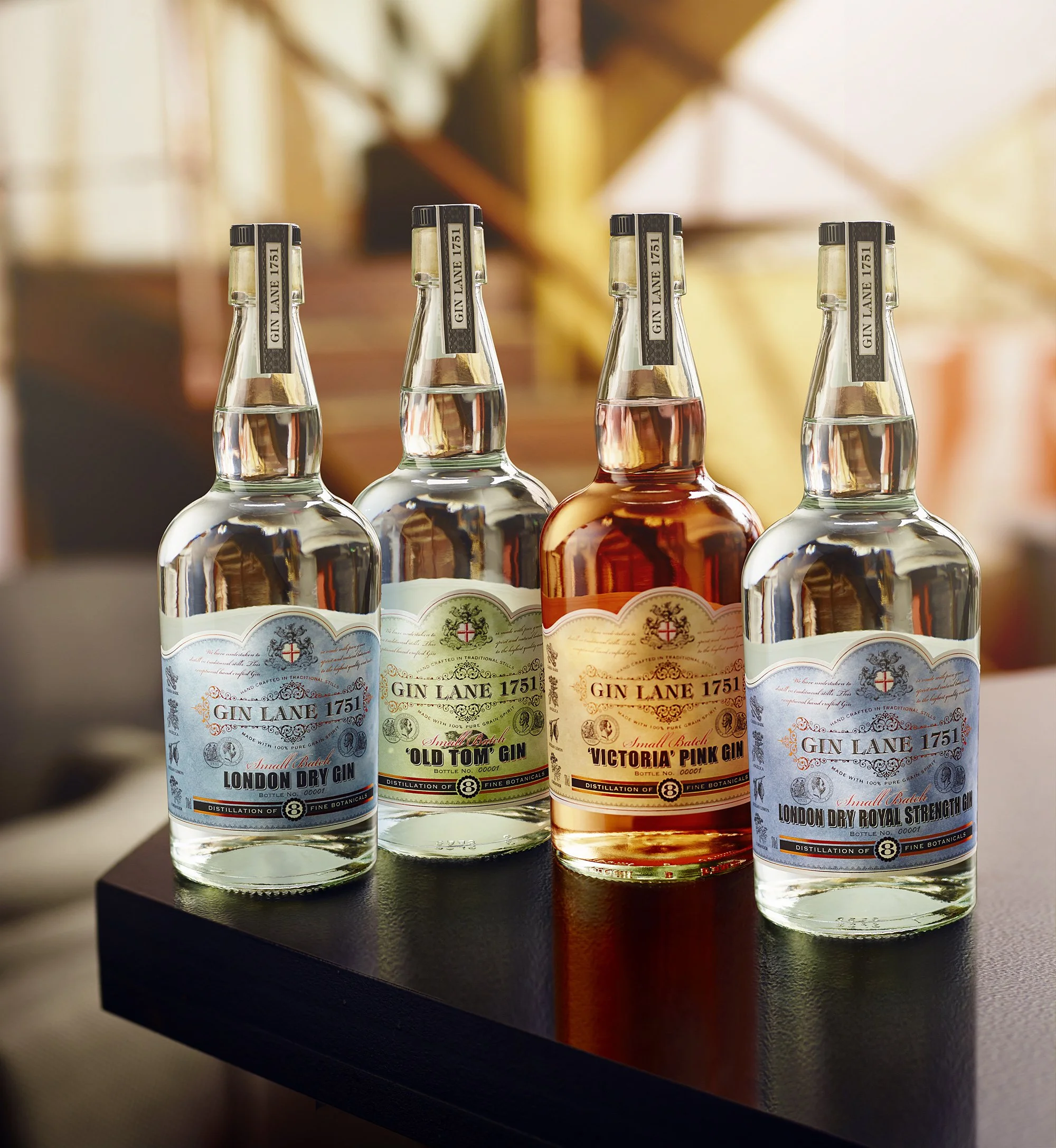 Four bottles of gin on a black surface with a blurred warm-toned background including wooden stairs.