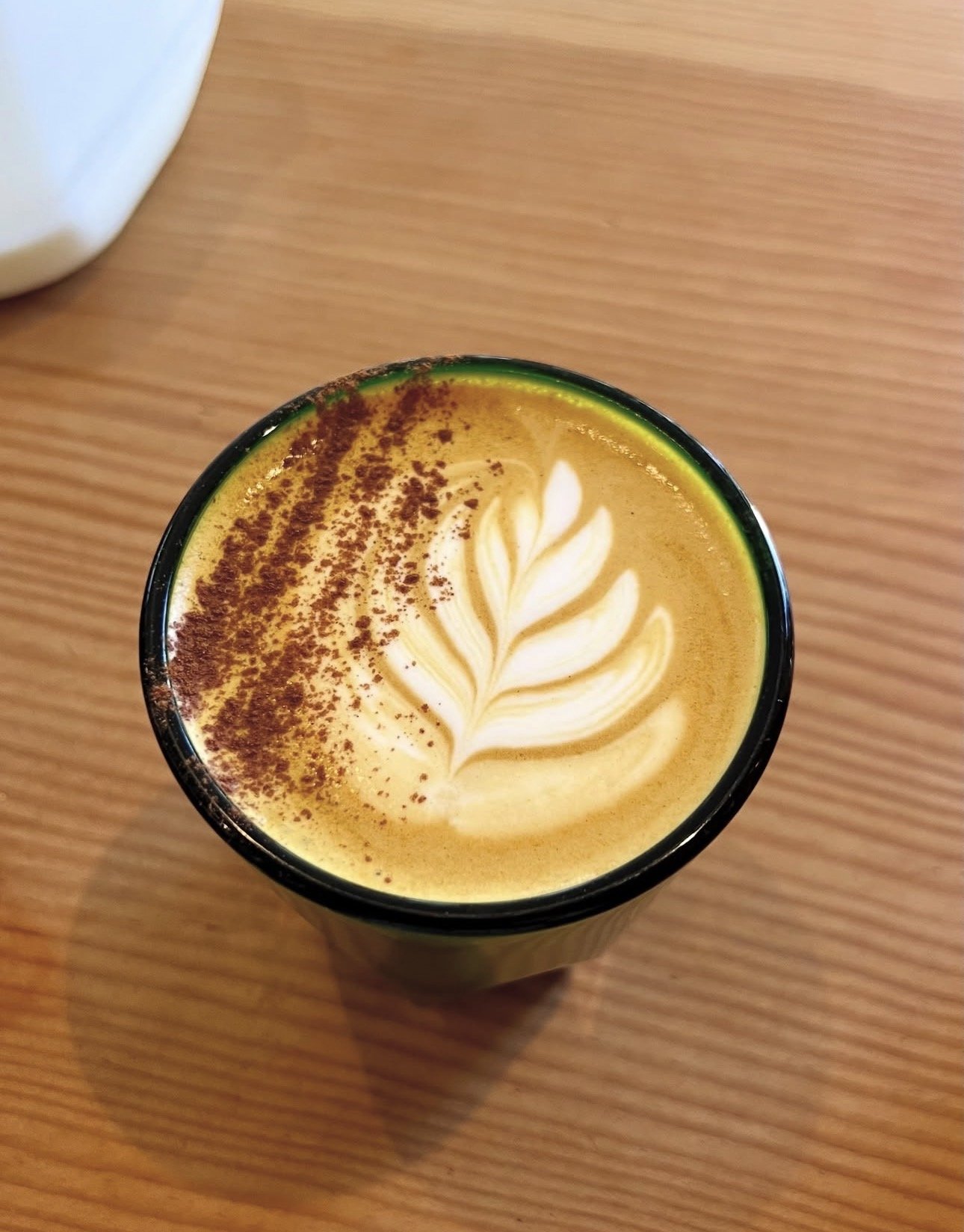 A cup of coffee with latte art in the shape of a leaf, sprinkled with cinnamon or cocoa powder on one side, on a wooden table.