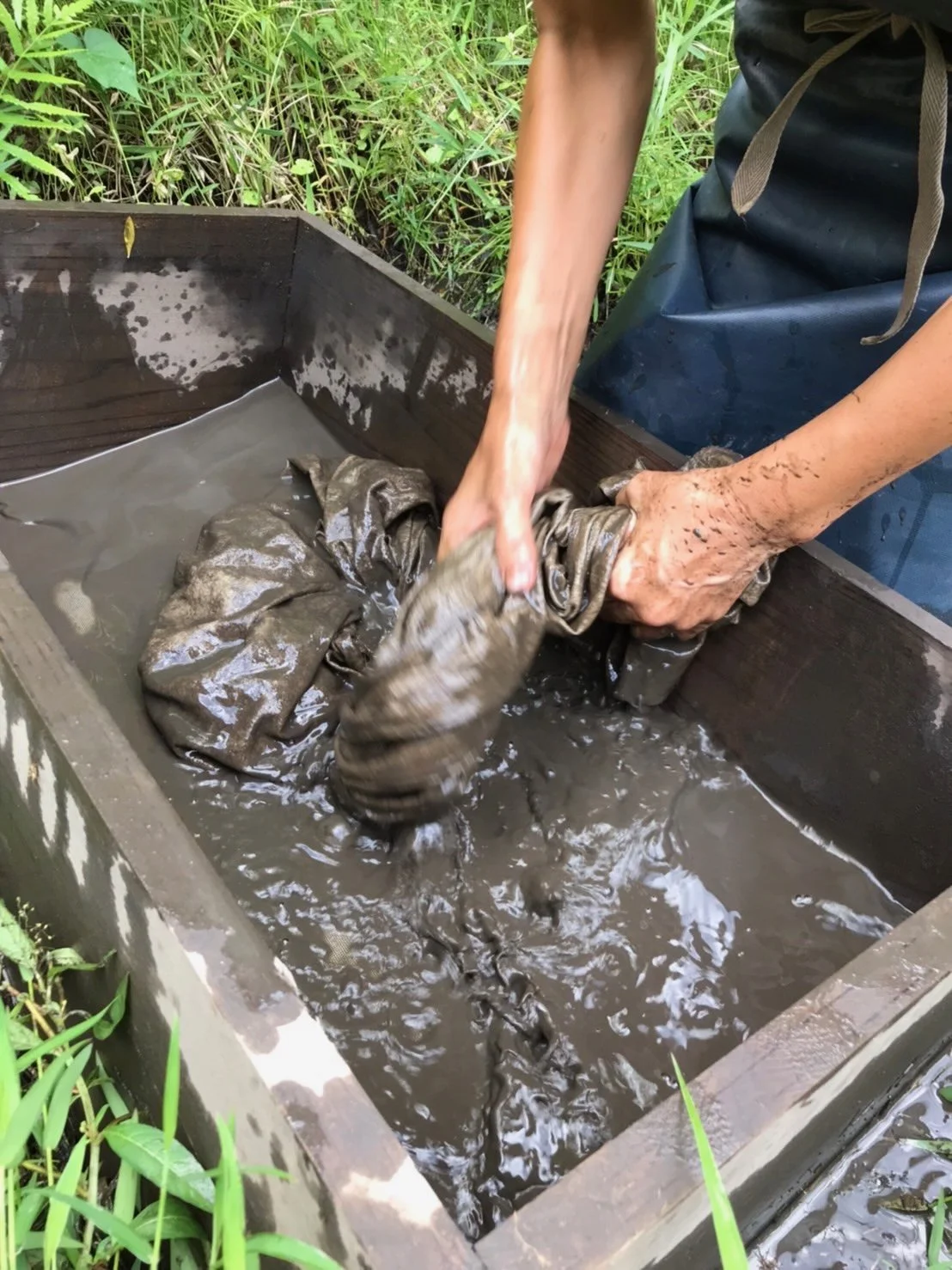 Hemp — mud-dye process.

After plant-dyeing, the cloth is washed in iron-rich island mud to set and deepen the color. These dyers in Amami Oshima carry one part of that chain.