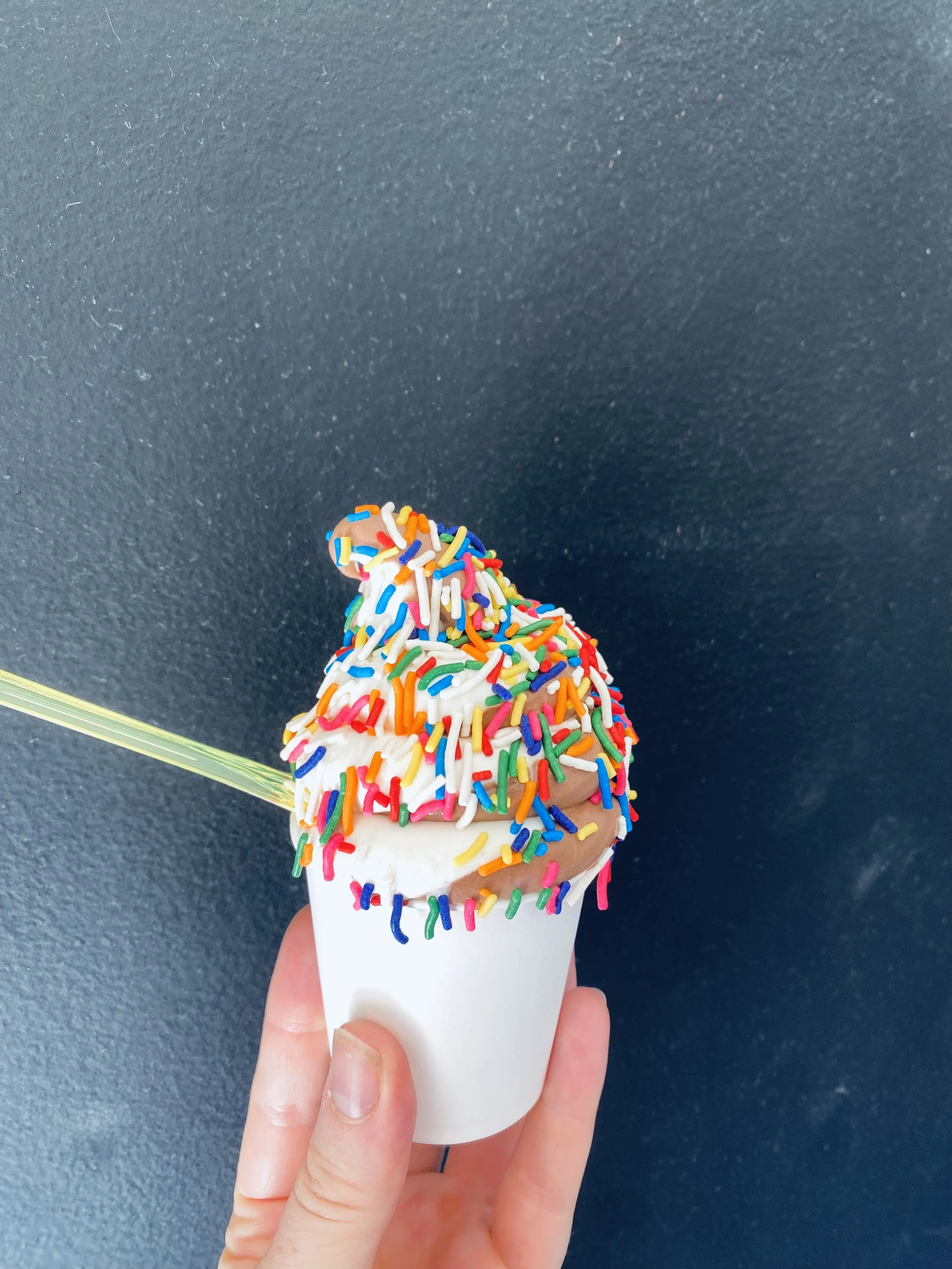 a chocolate and vanilla swirl of soft serve with rainbow sprinkle against a black background