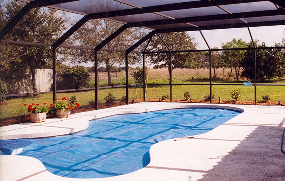 Free form shaped pool with blue solar pool cover on it