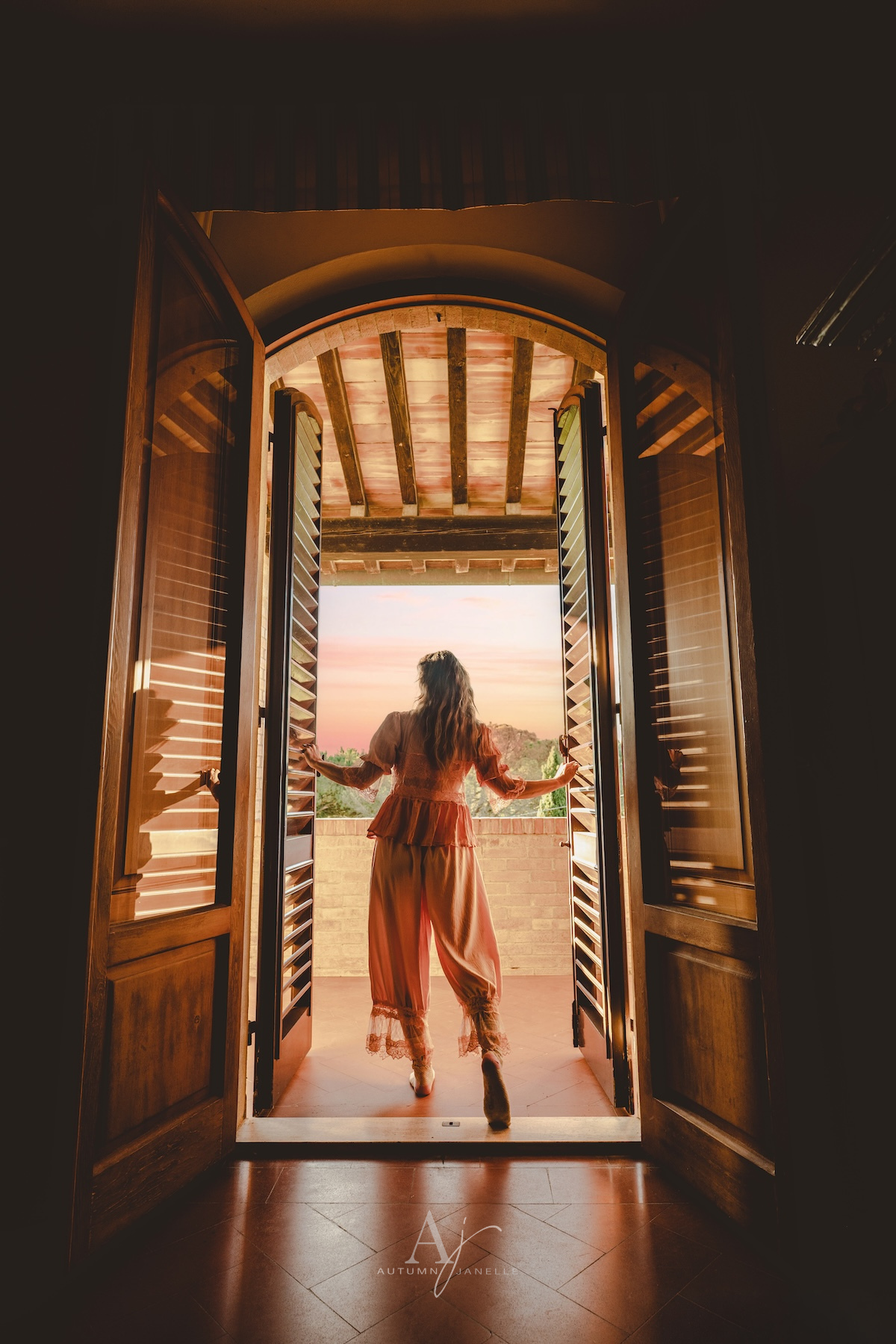 Woman in pajamas looking out window at sunrise in San Gimignano at Villa Raccienello in Italy