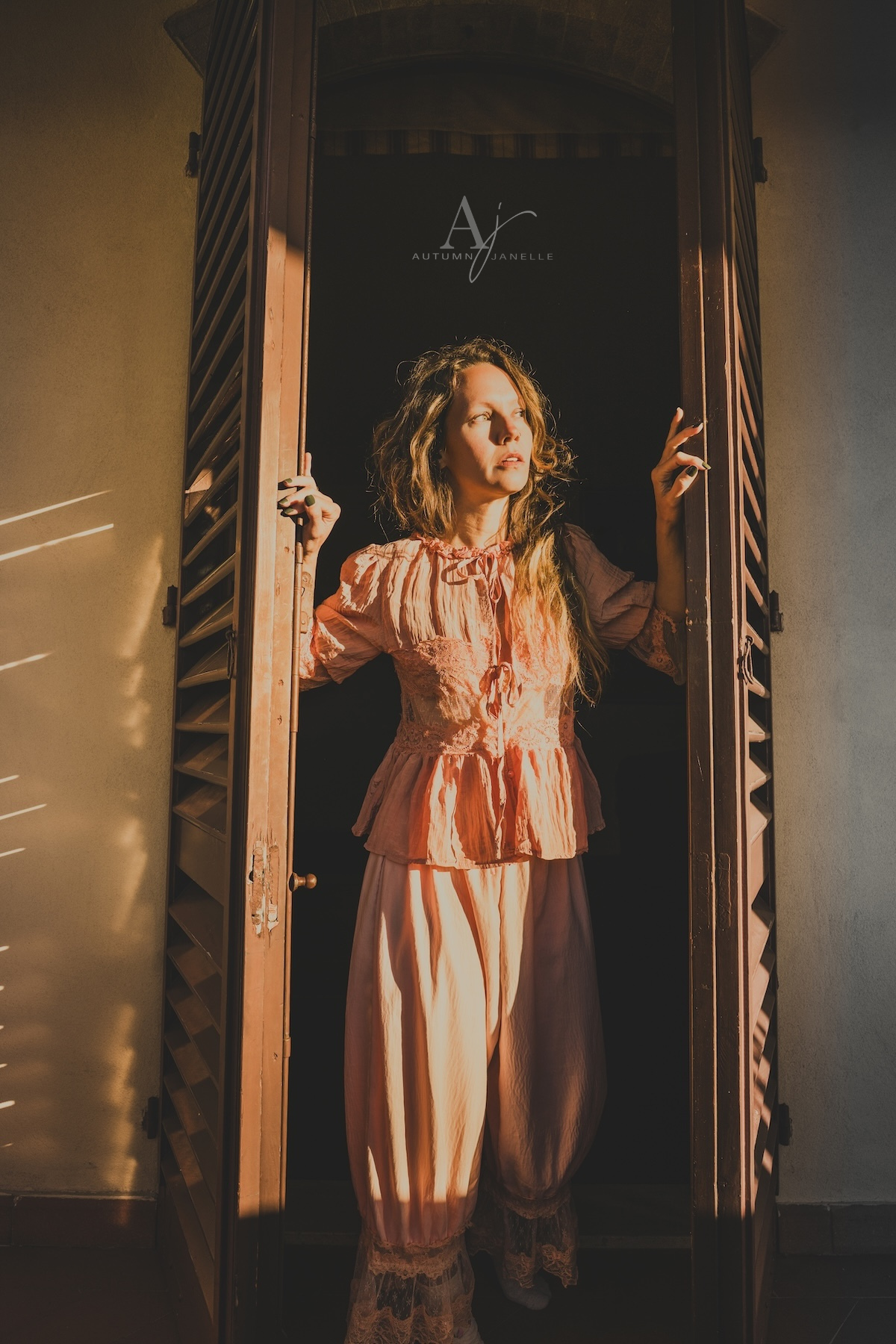 Woman in pajamas looking out window at sunrise in San Gimignano at Villa Raccienello in Italy