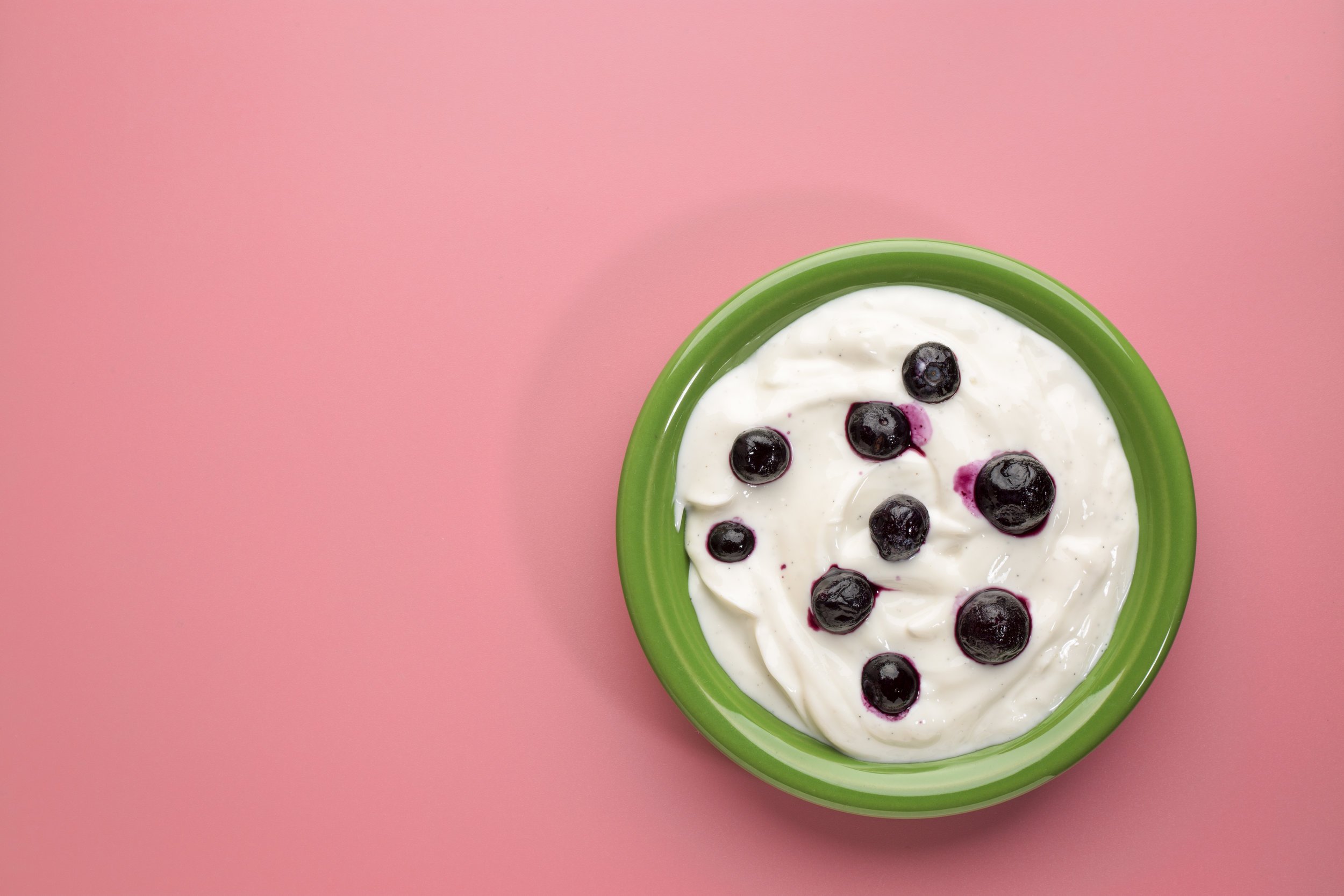 a bowl of yogurt and blueberries on a pink background