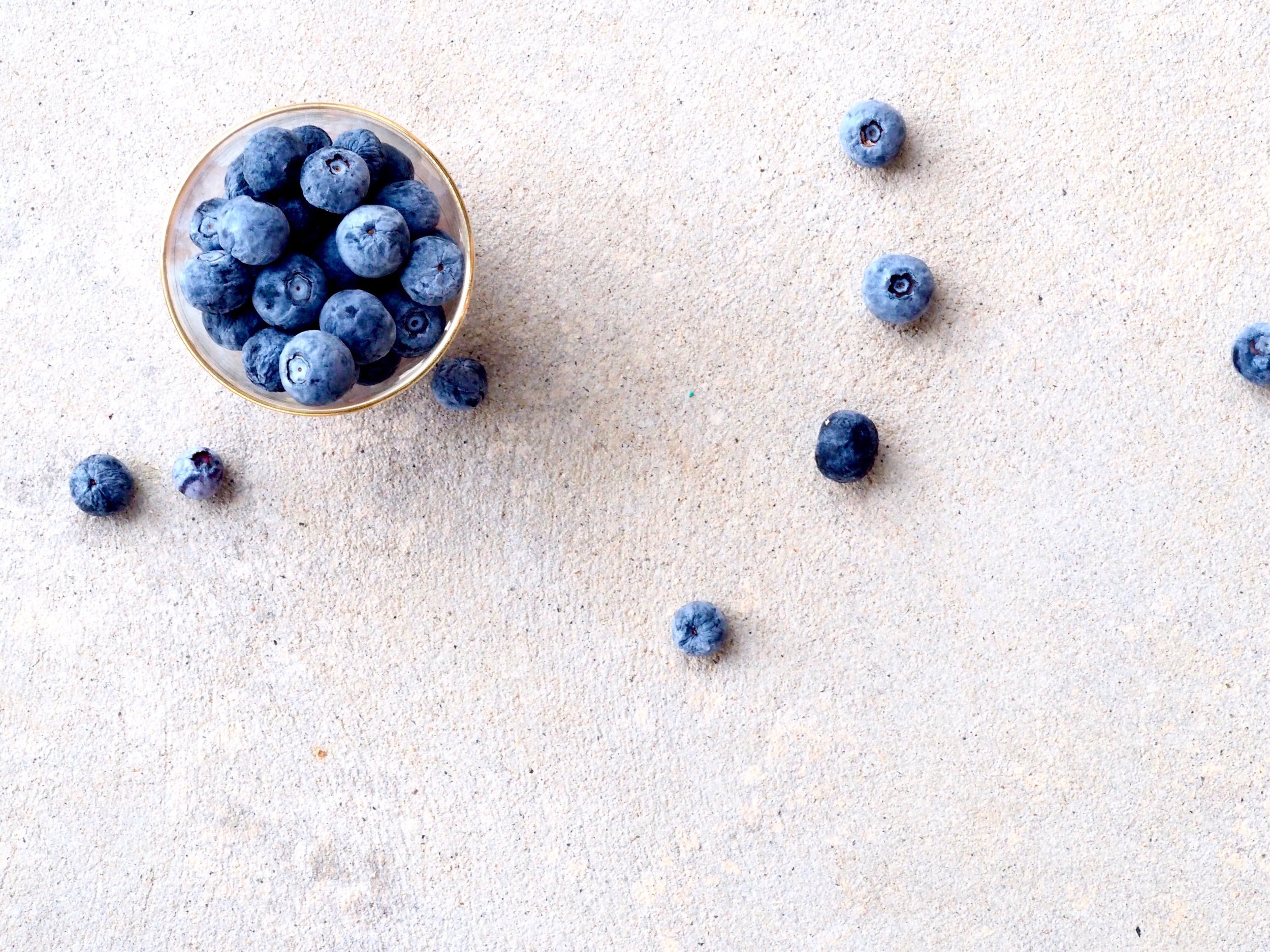 a cup of blueberries with some scattered around