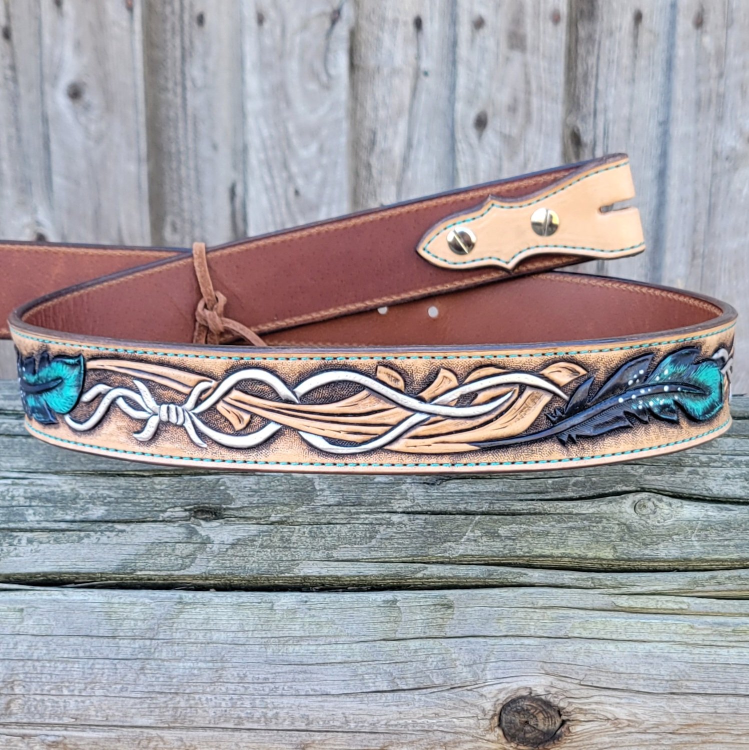 Custom leather belt designed with feather and barb wire hand tooling.