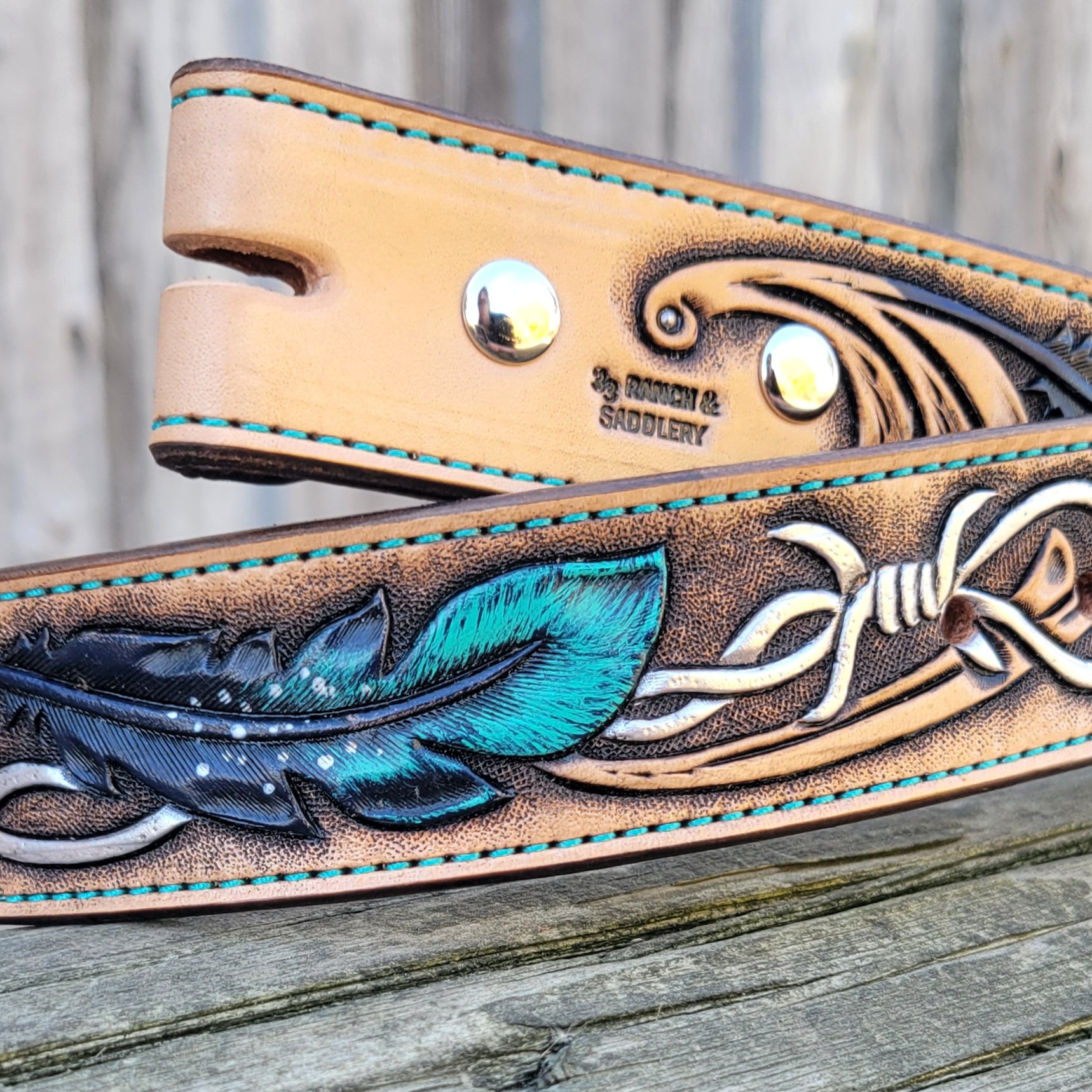 Closeup of hand tooled feather and barb wire design on a custom leather belt.
