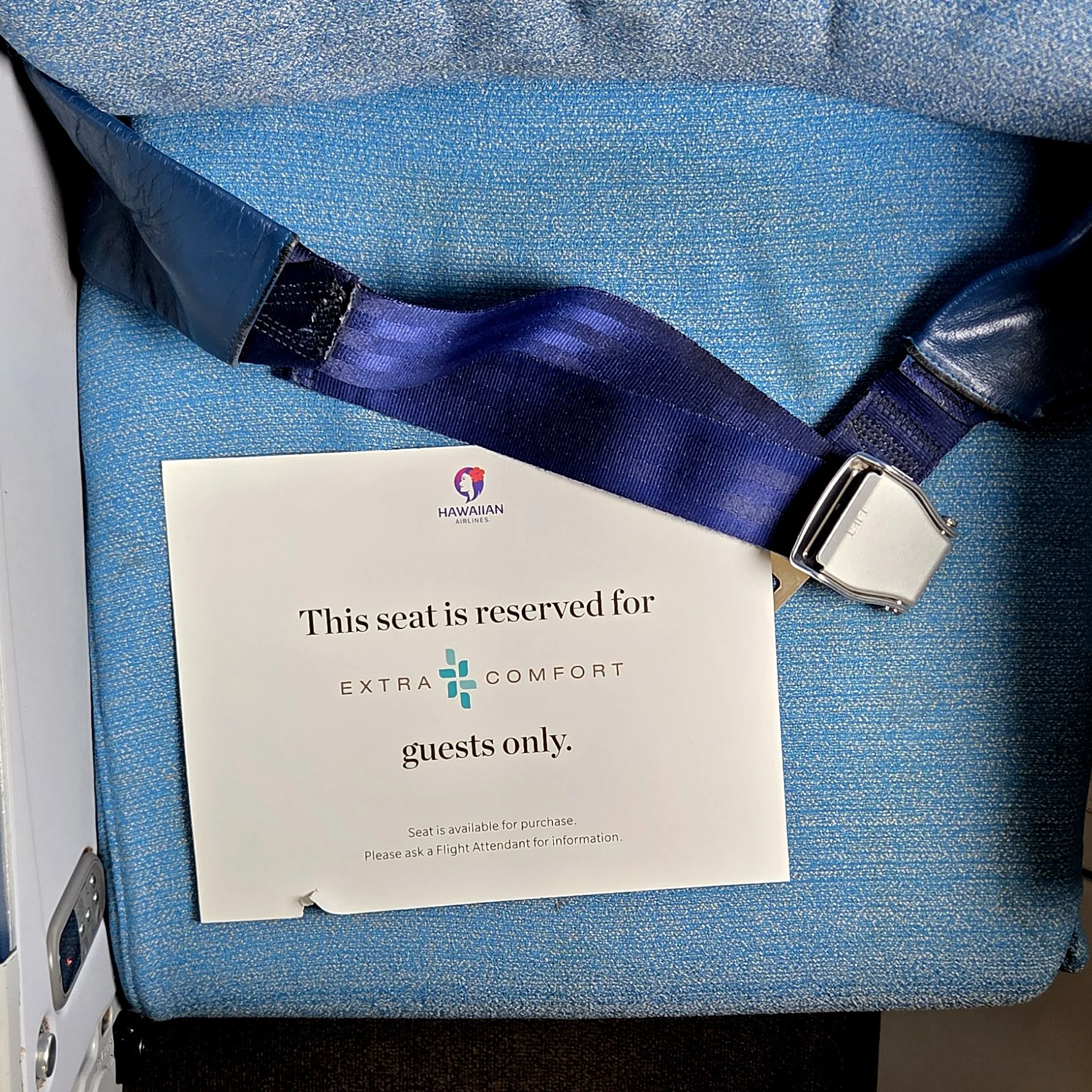 Overhead photo of an airline seat that has a sign sitting on it that says "This seat is reserved for Extra Comfort Guests Only"