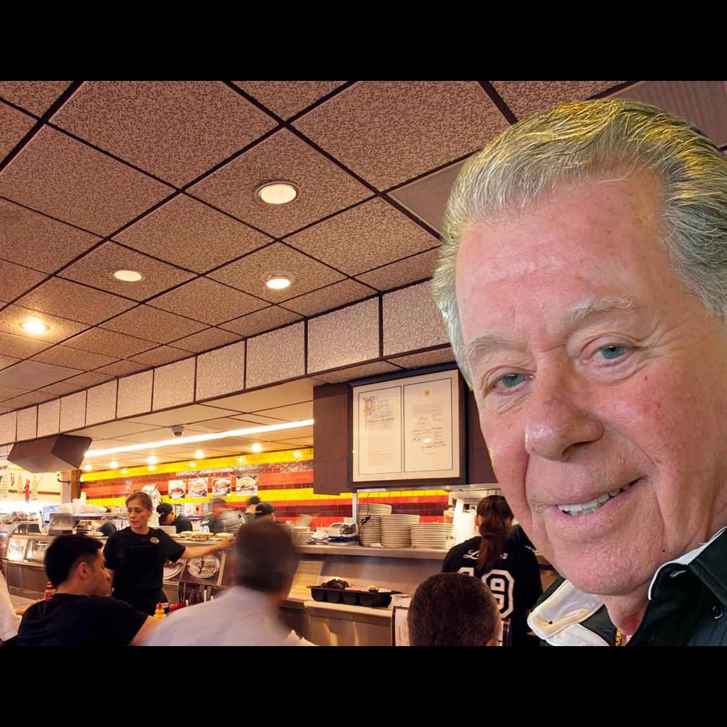 Photo of Norm Langer, the owner of Langer's Deli, in his restaurant. You can see the counter and customers behind him