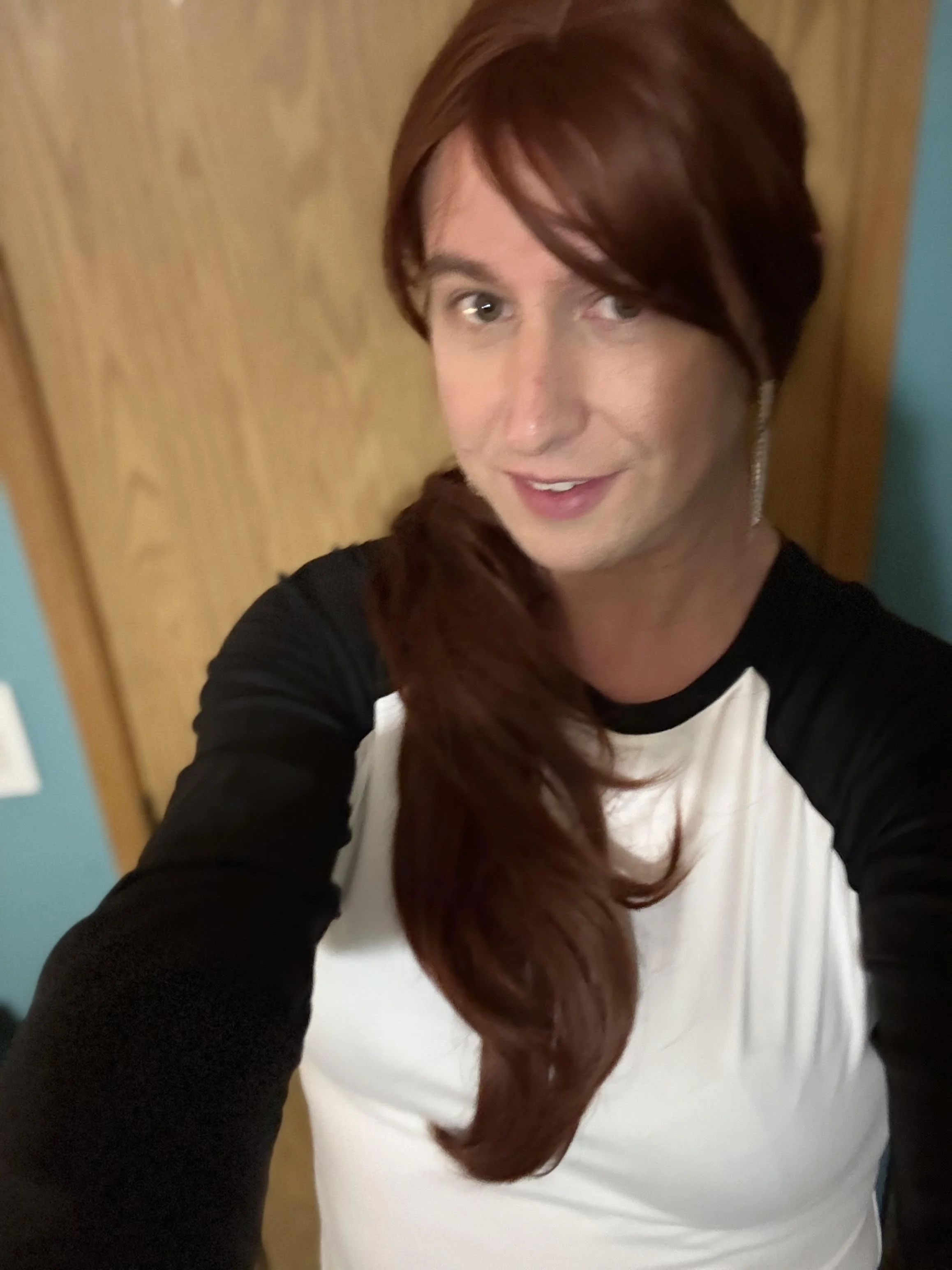 Stacia Colasurdo takes a selfie with a door behind her, as she wears a raglan tee-shirt similar to the TBTL Jr. Slugger baseball tees.