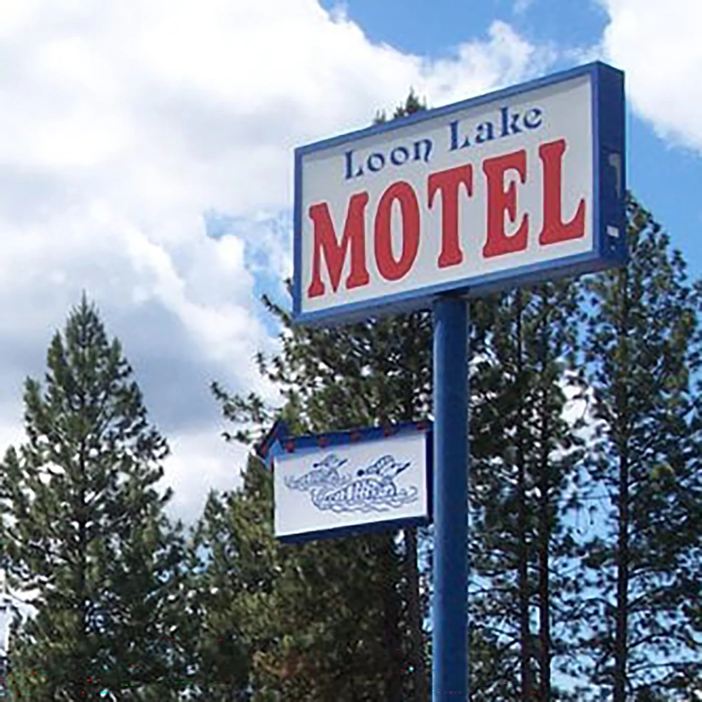 Photo of a basic sign on a pole that says "Loon Lake MOTEL" with trees in the background