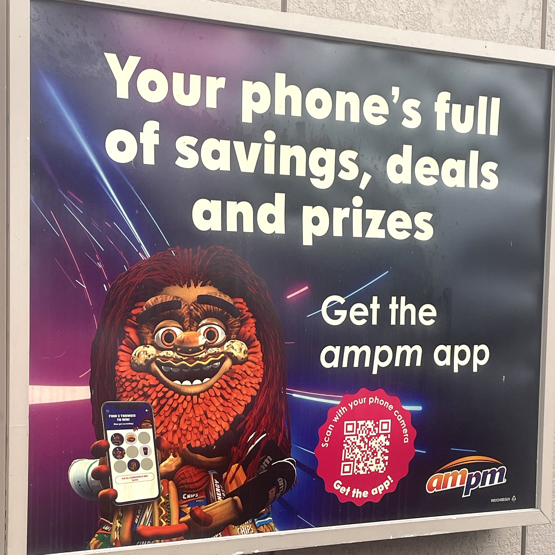 Photo of a sign outside an AMPM showing the AMPM mascot, Toomgis, holding a phone. Text says "Your phone's full of savings, deals and prizes - get the ampm app"
