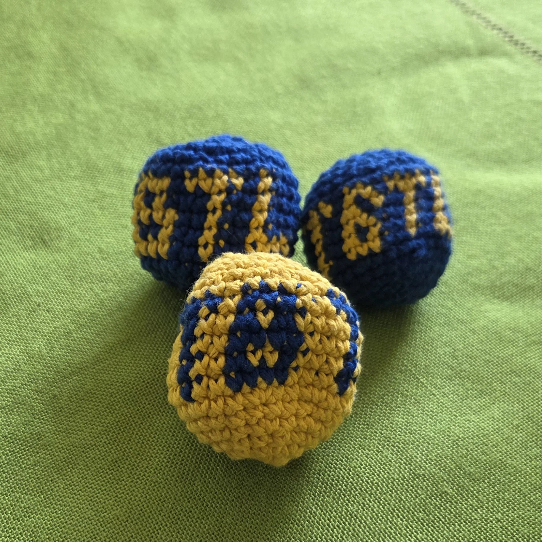 photo of three hand-crocheted hacky sacks that say TBTL on them. They  are blue and yellow.