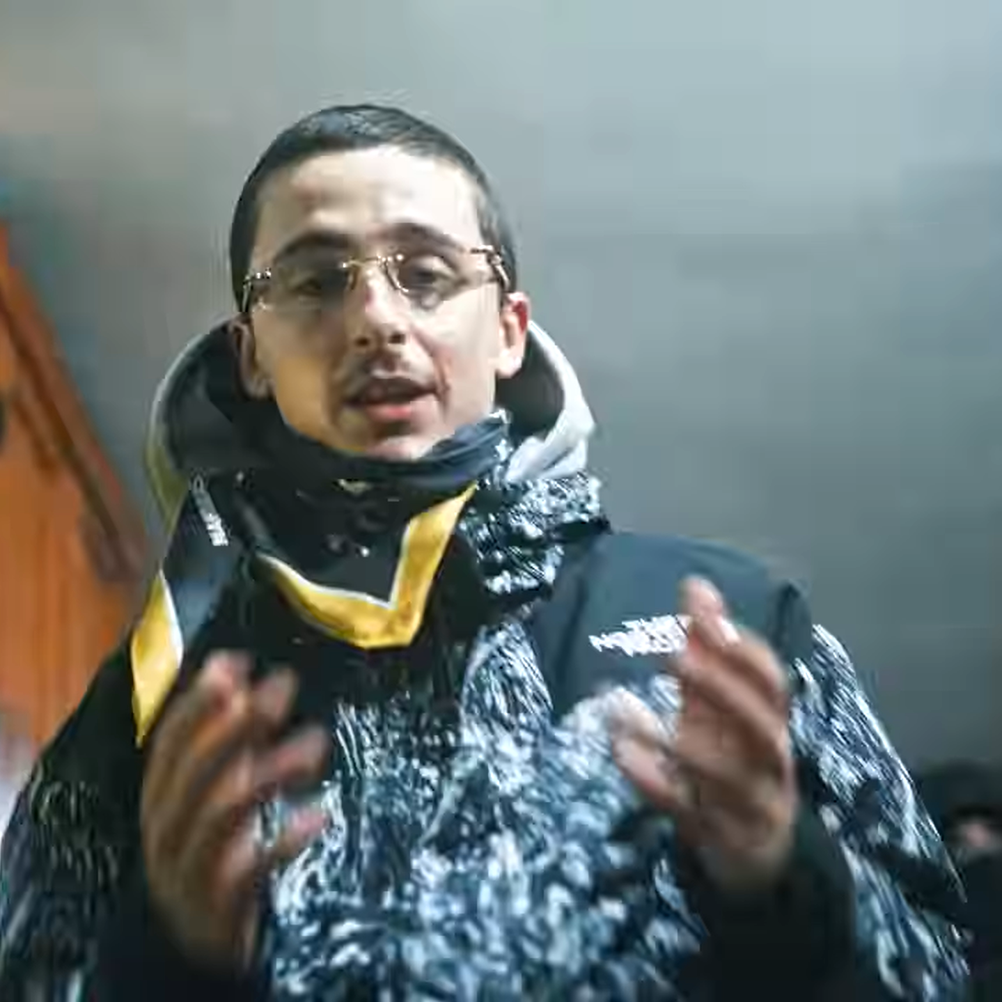 still shot of timothee chalamet from a music video. He is wearing street wear and rapping into the camera.