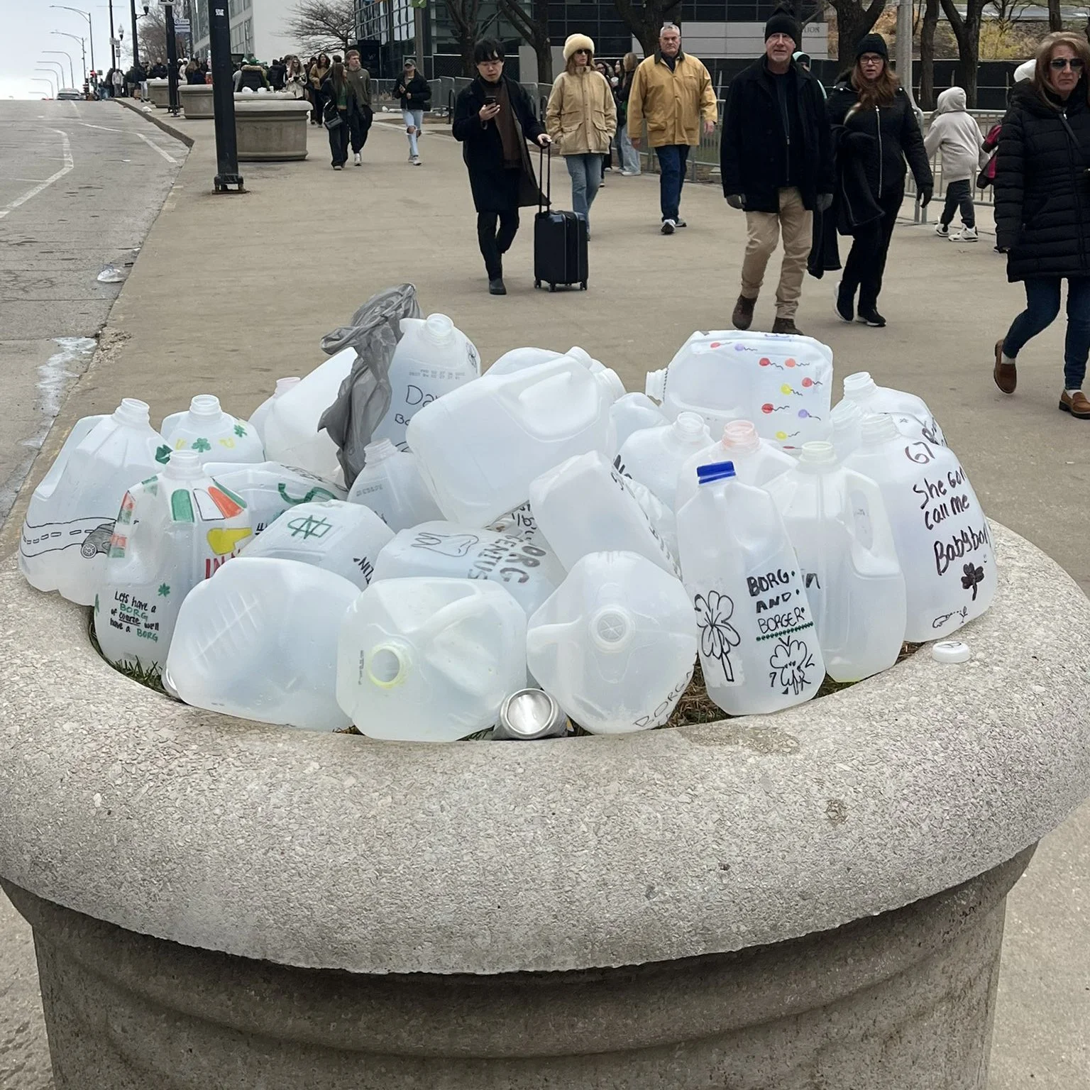Photo of a public garbage can in Chicago that is overflowing with old milk cartons that were used for drinking green booze
