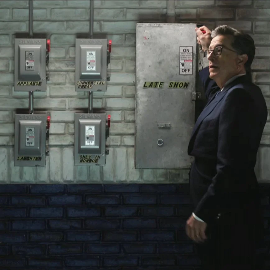Image of Stephen Colbert throwing a "Late Show" off switch mounted on a brick wall. It's from one of the final scenes on the last episode of the Late Show