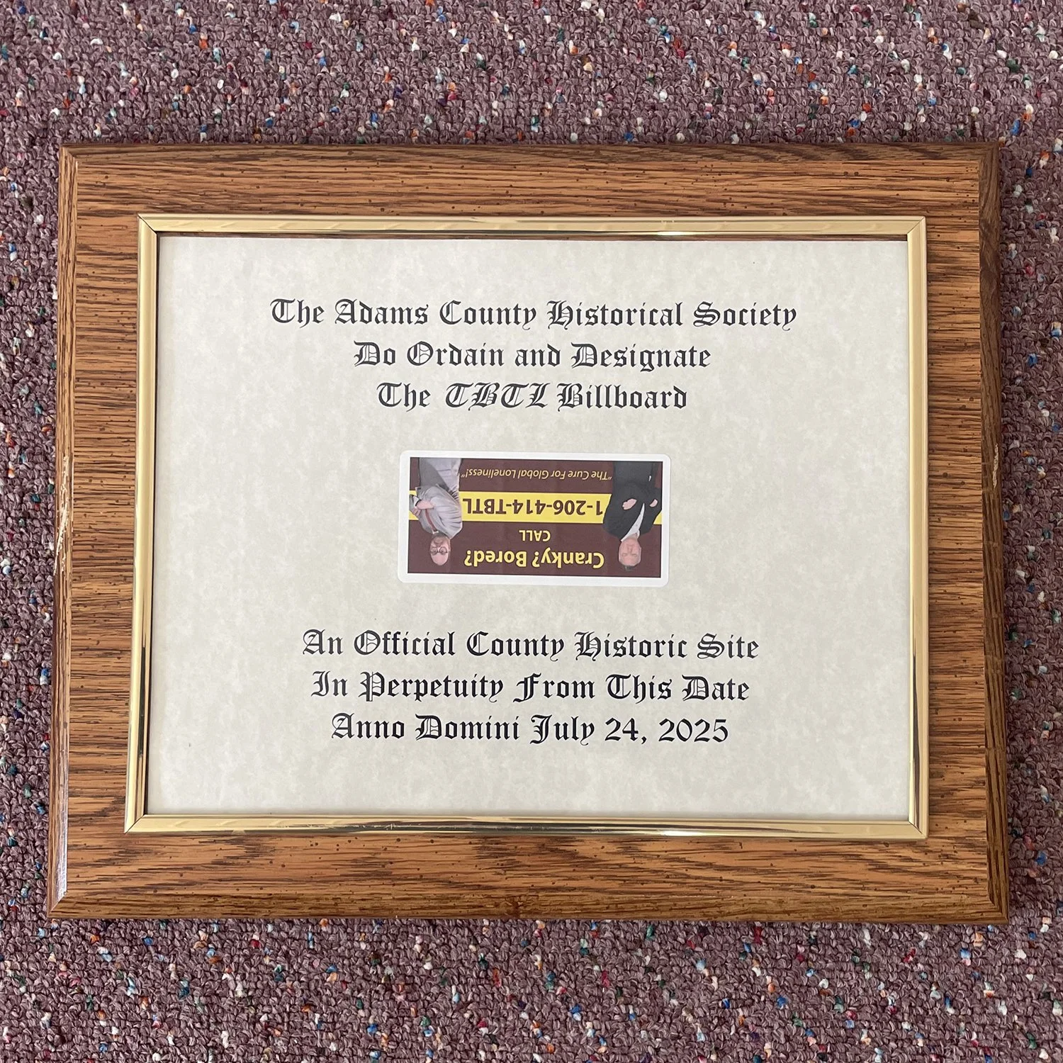 Plaque that says "The Adams County Historical Society Do Ordain and Designate the TBTL Billboard An Official County Historic Site in Perpetuity From This Date Anno Domini July 24, 2025