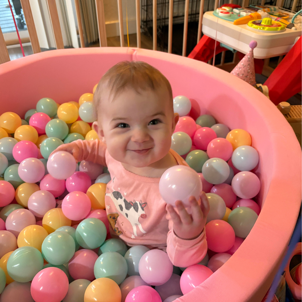 Gemma, daughter of DFTB and niece to Luke, smiles while sitting in a ball pit.