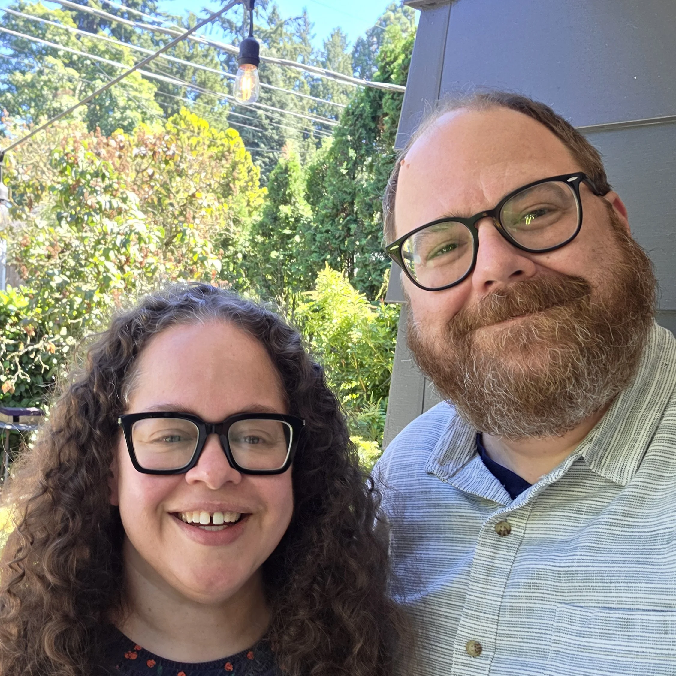 Photo of Phyllis and Andrew standing outside Andrew's front door. You see a tiny bit of the siding in the background, but mostly greenery in the yard.