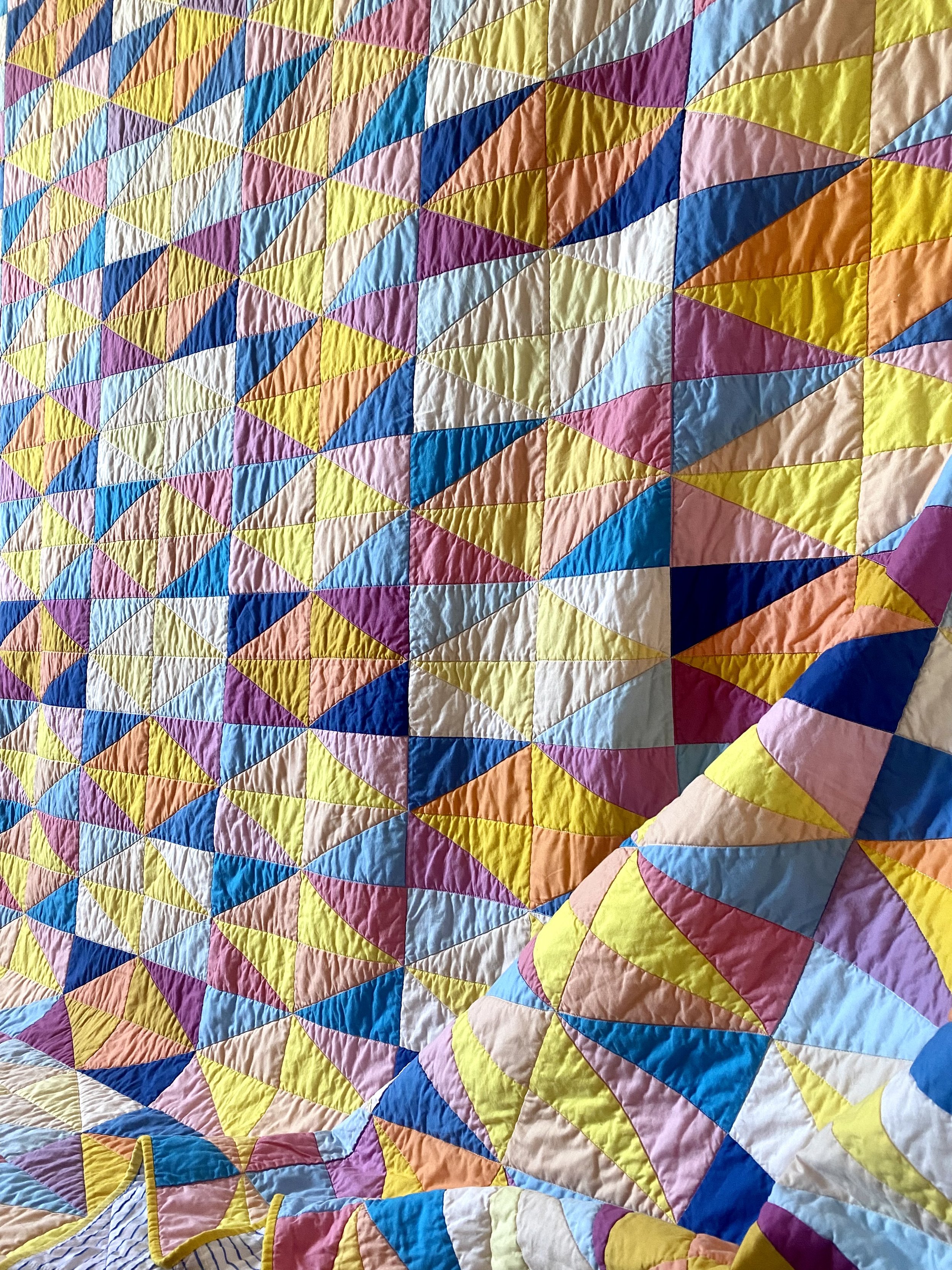 An angled view of the quilt, highlighting the quilted texture, and the repeating pattern of the triangles-in-a-diamond quilt blocks, made in shades and tints of the same colors.