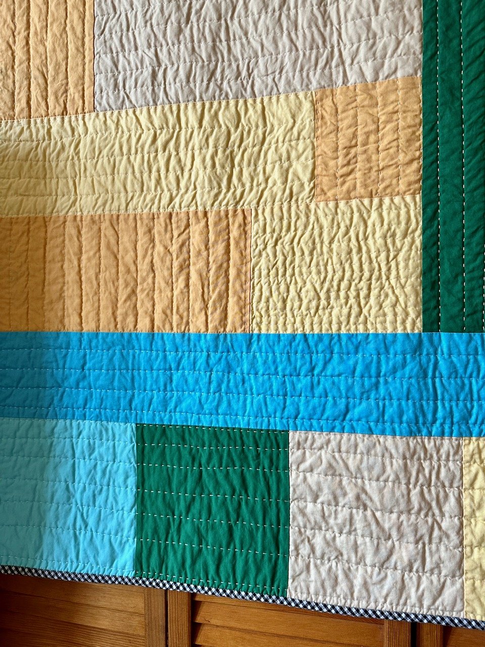 Close up of big stitch hand quilting on a blue and green improv patchwork quilt