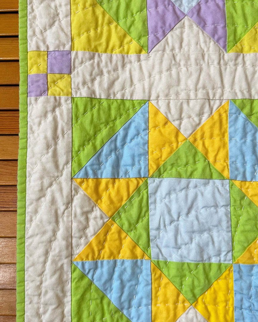 Close up of the edge of the quilt, highlighting a 4-patch sashing cornerstone and chartreuse colored binding along the edge