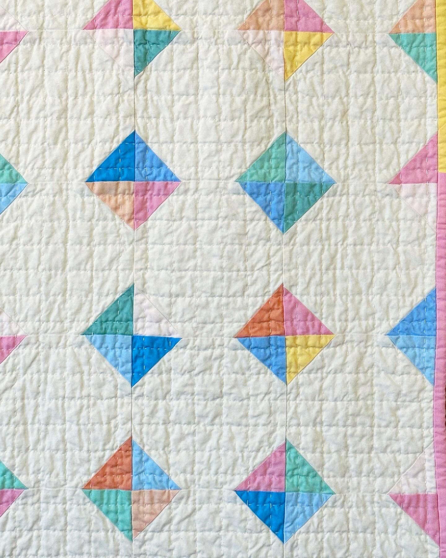 A close up of the snowball blocks with hand quilted grid running across them, and a hint of the pink and yellow patchwork binding visible at the edge.