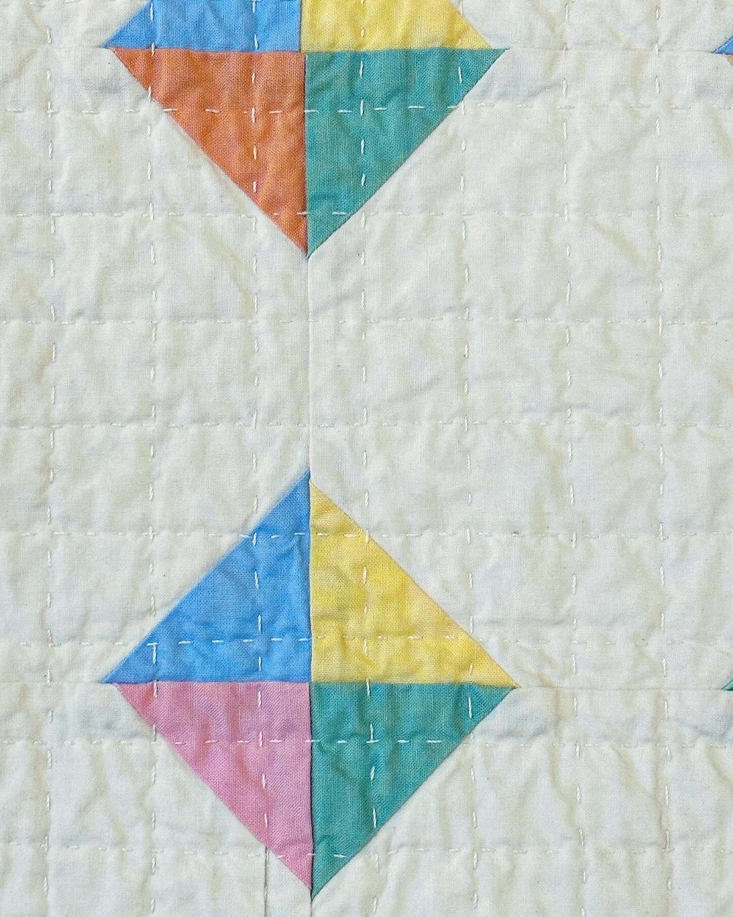 Very close up on the hand quilted grid and the colorful diamonds meeting at the corners of several patchwork blocks