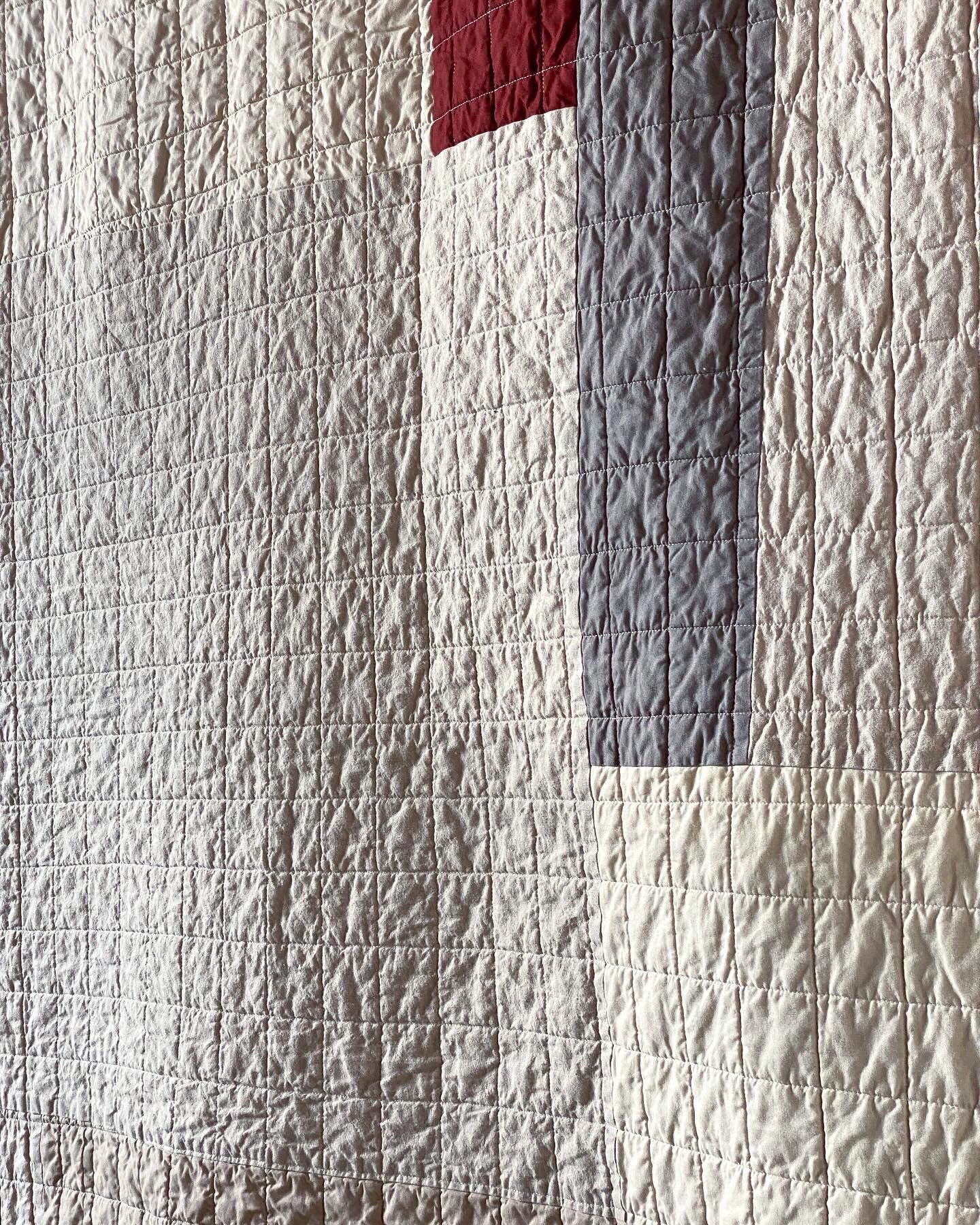 A side angle of the quilt, hanging, the light catching the quilted grid and showing lots of crinkly texture along the cotton and linen patchwork