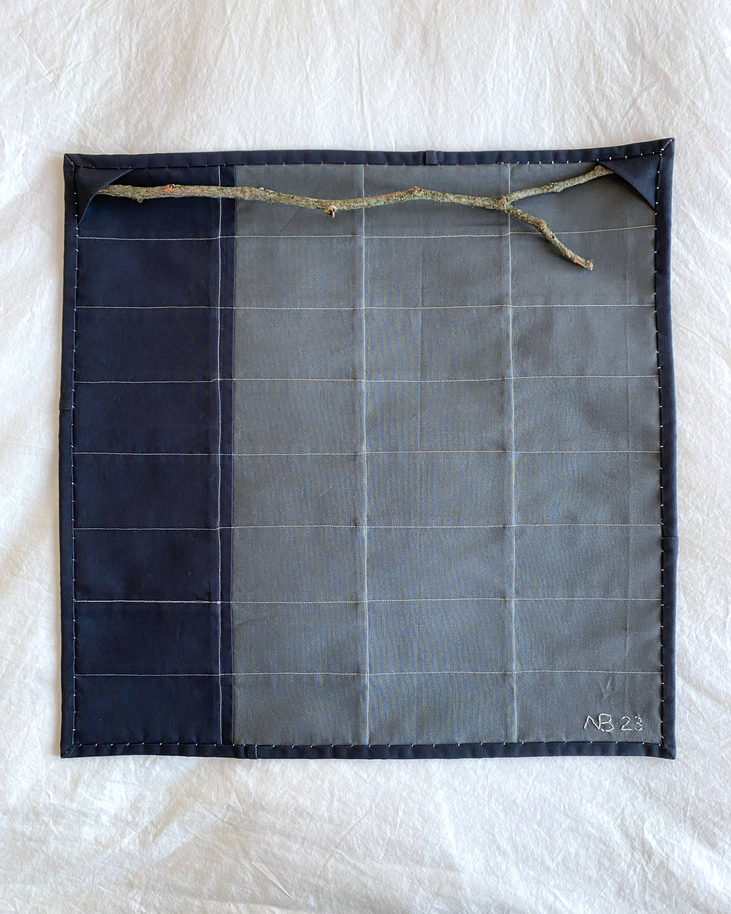 Back of the wall hanging showing the hanging method - pocket triangles and a stick from a tree used as the hanging rod
