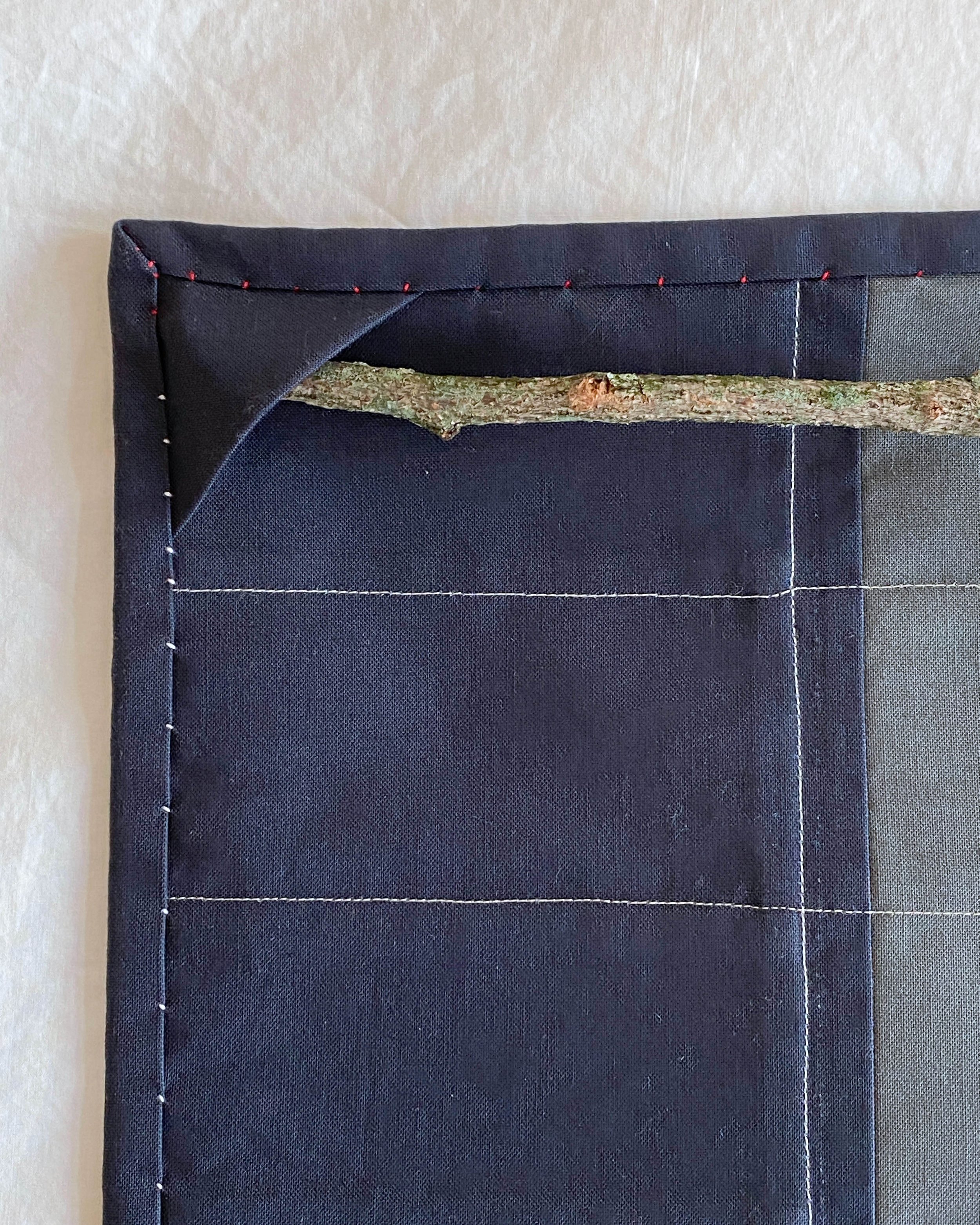 Close up of a stick tucked in to the hanging corner on the back of the quilted wall hanging