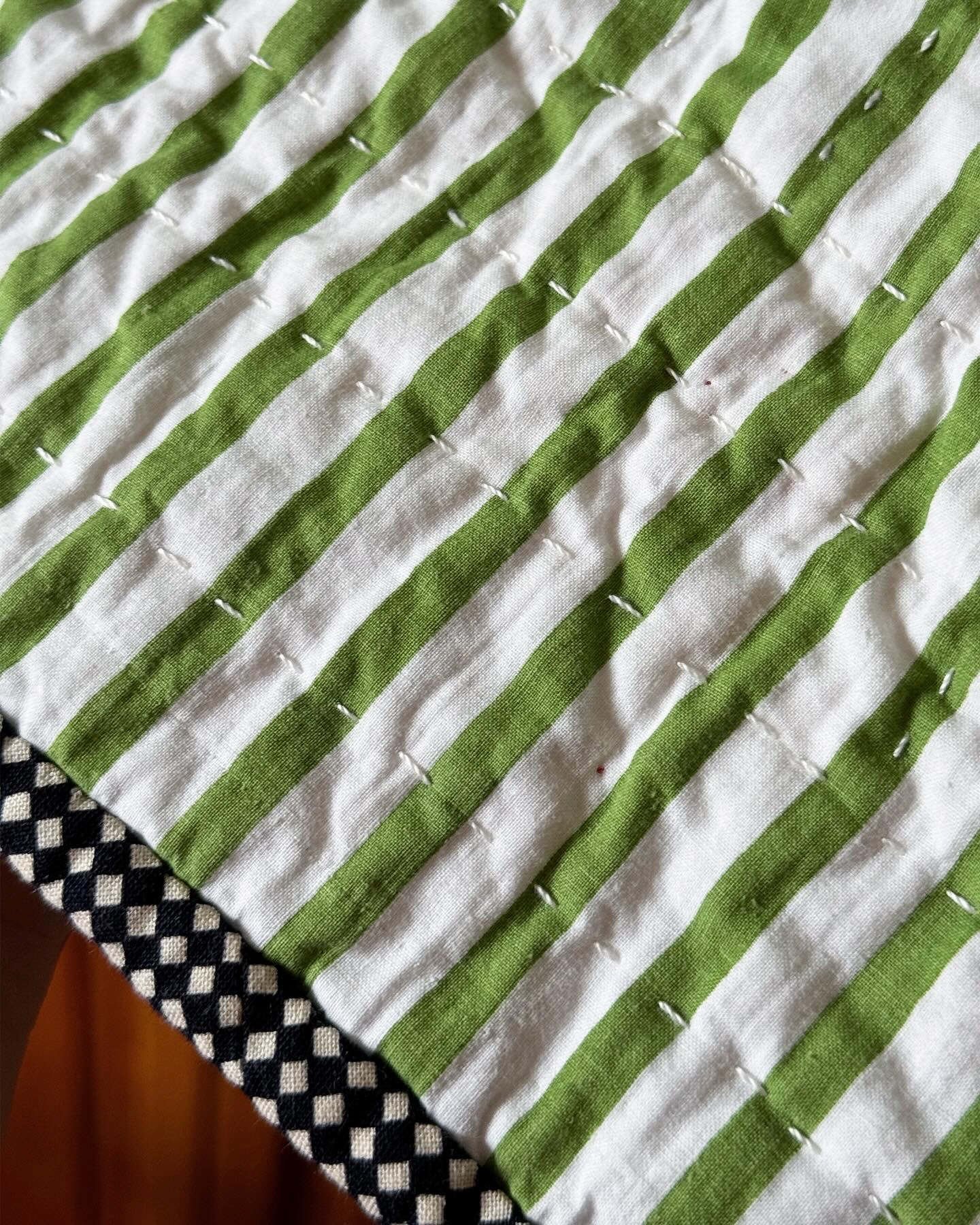 Close up of the green and white striped fabric and the black and ivory checkerboard binding.