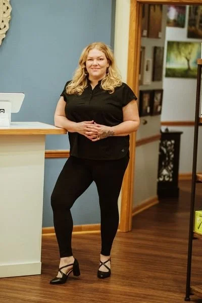 Anna wearing a black top and black pants standing in the studio's reception area