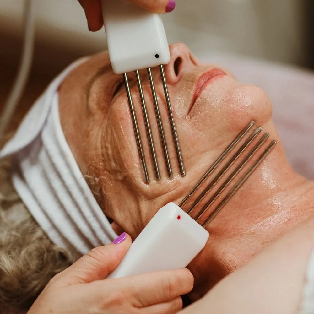 Aesthetician performing microcurrent sculpting facial in Buffalo on an elderly woman's face with metal probes.
