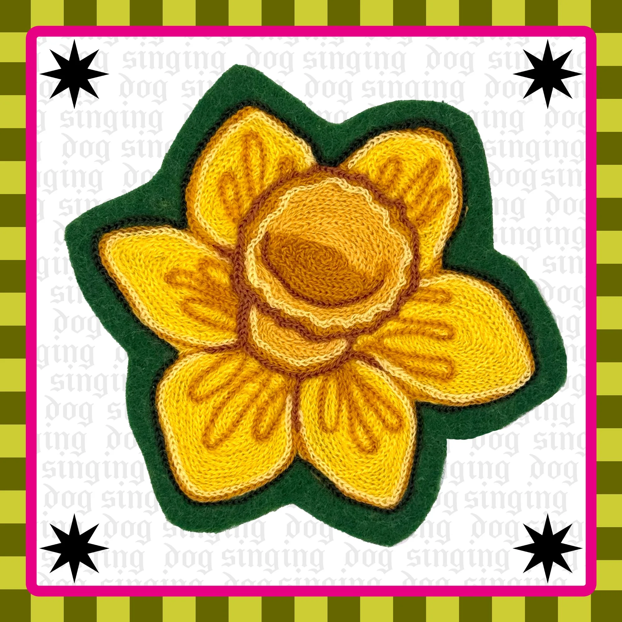 A yellow chainstitch embroidered daffodil on green felt, the background is white with a pink border and black starburst designs.