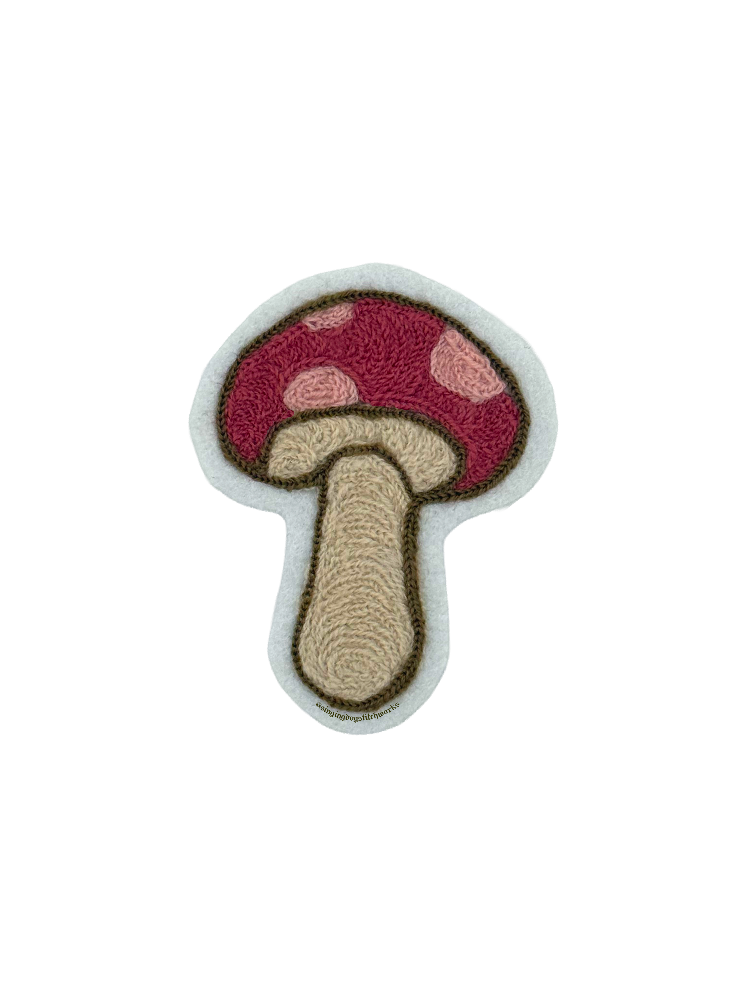 A handmade embroidery patch in the shape of a red mushroom with pink spots and a beige stem, outlined with brown stitching.